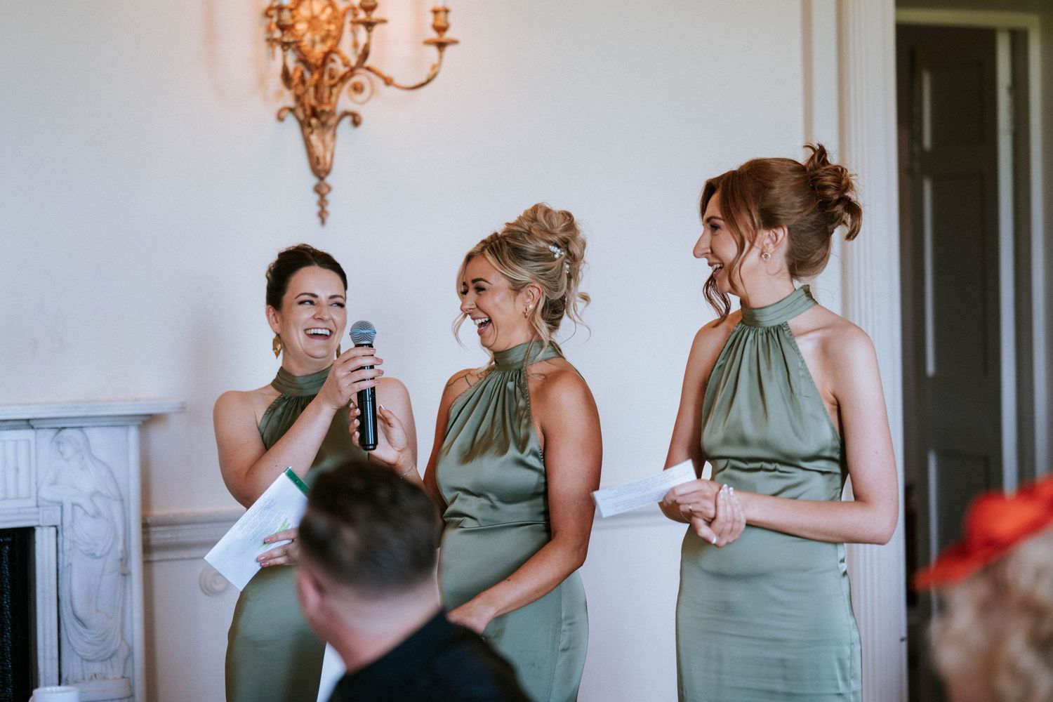 Fasque Castle Wedding Photography. Wedding party members in sage green dresses share laughter and drinks at an elegant reception.
