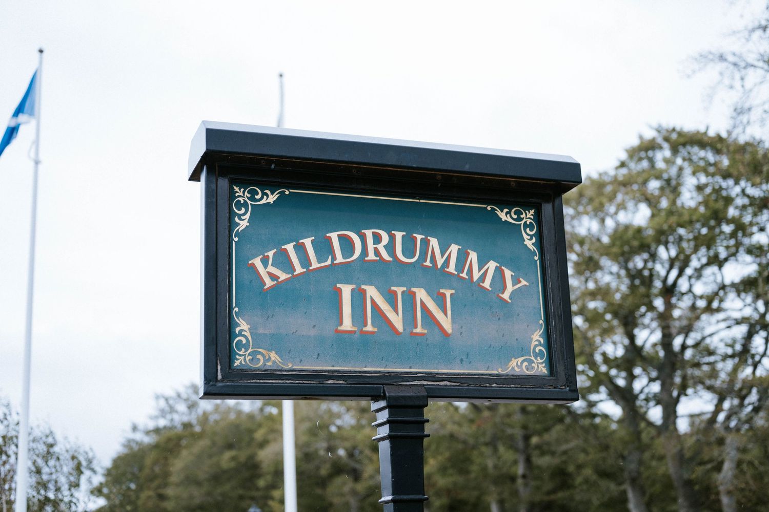 Exterior view of Kildrummy Inn with signage and trees visible against cloudy sky.