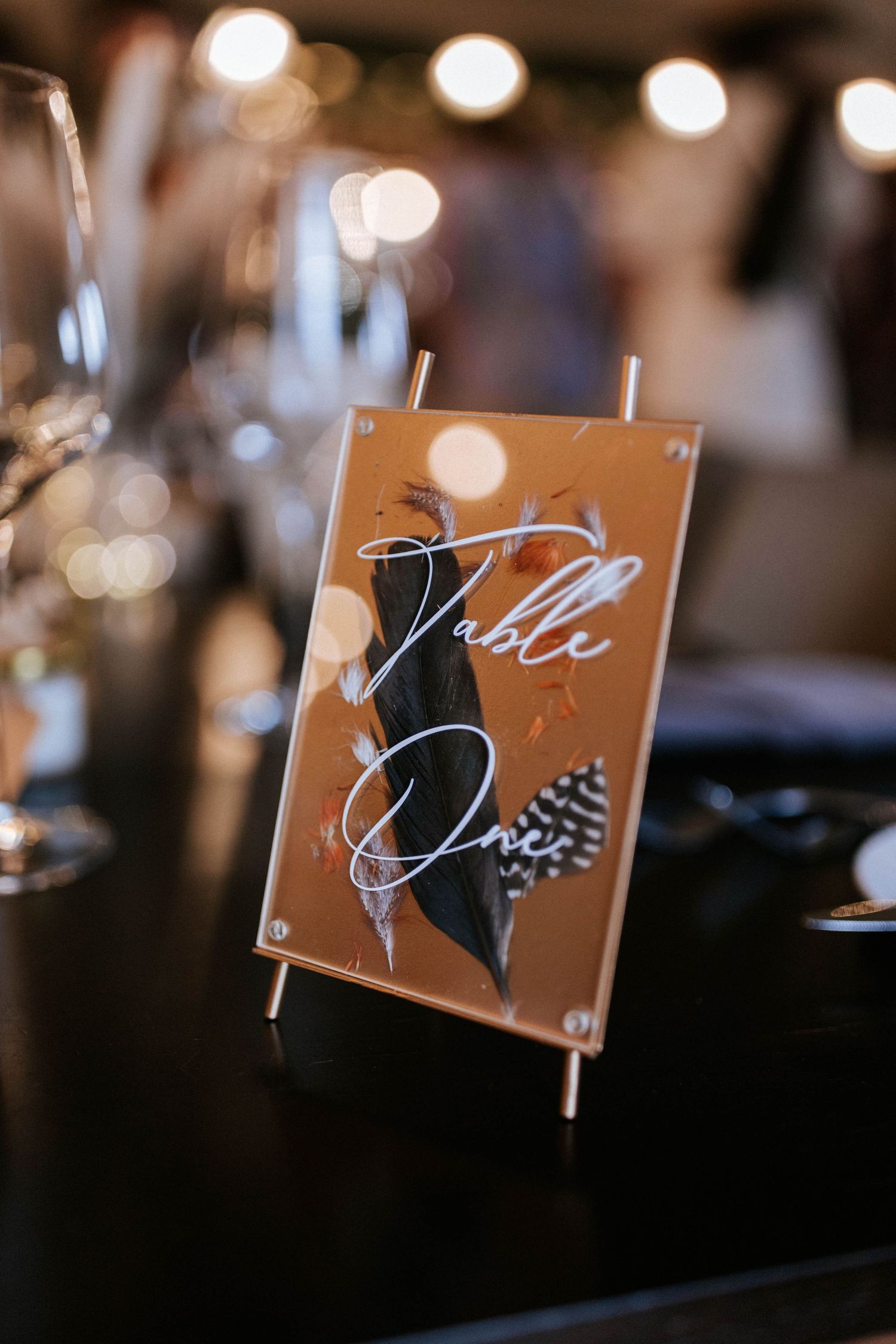 Wooden table number signs with elegant calligraphy displayed against blurred bokeh lights.