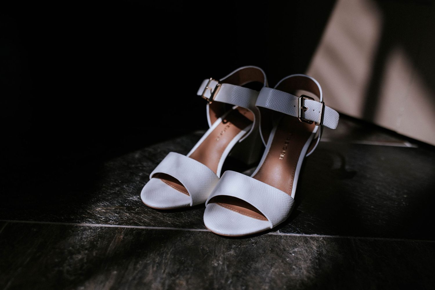 Light blue wedding heels photographed on dark surface with dramatic lighting.