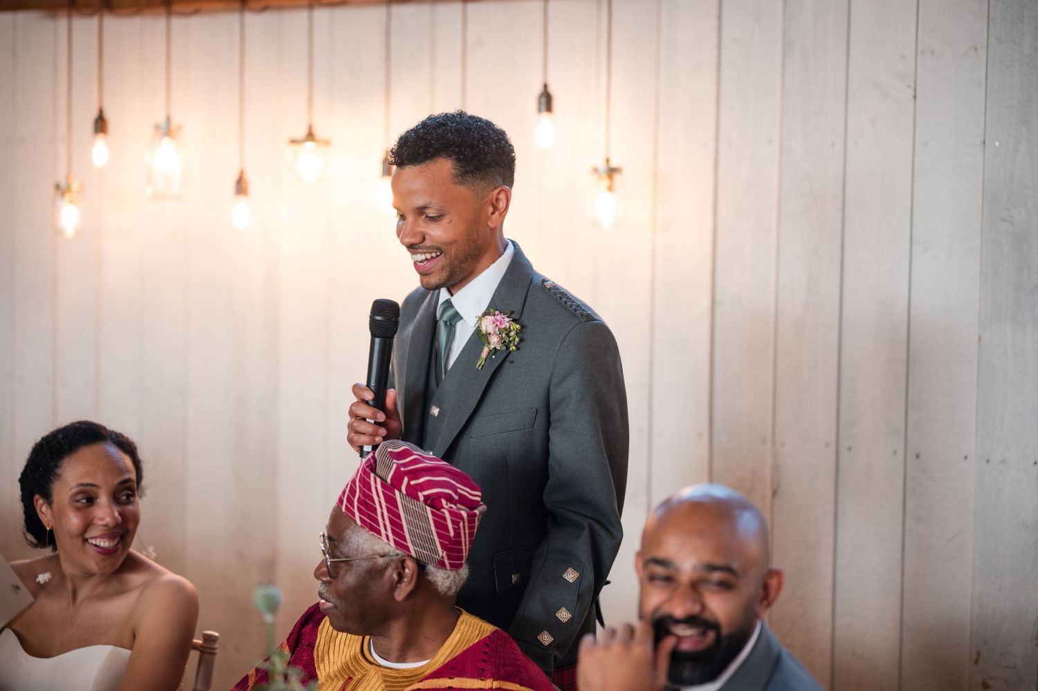 Wedding reception in rustic venue with white wood paneling and pendant lighting.