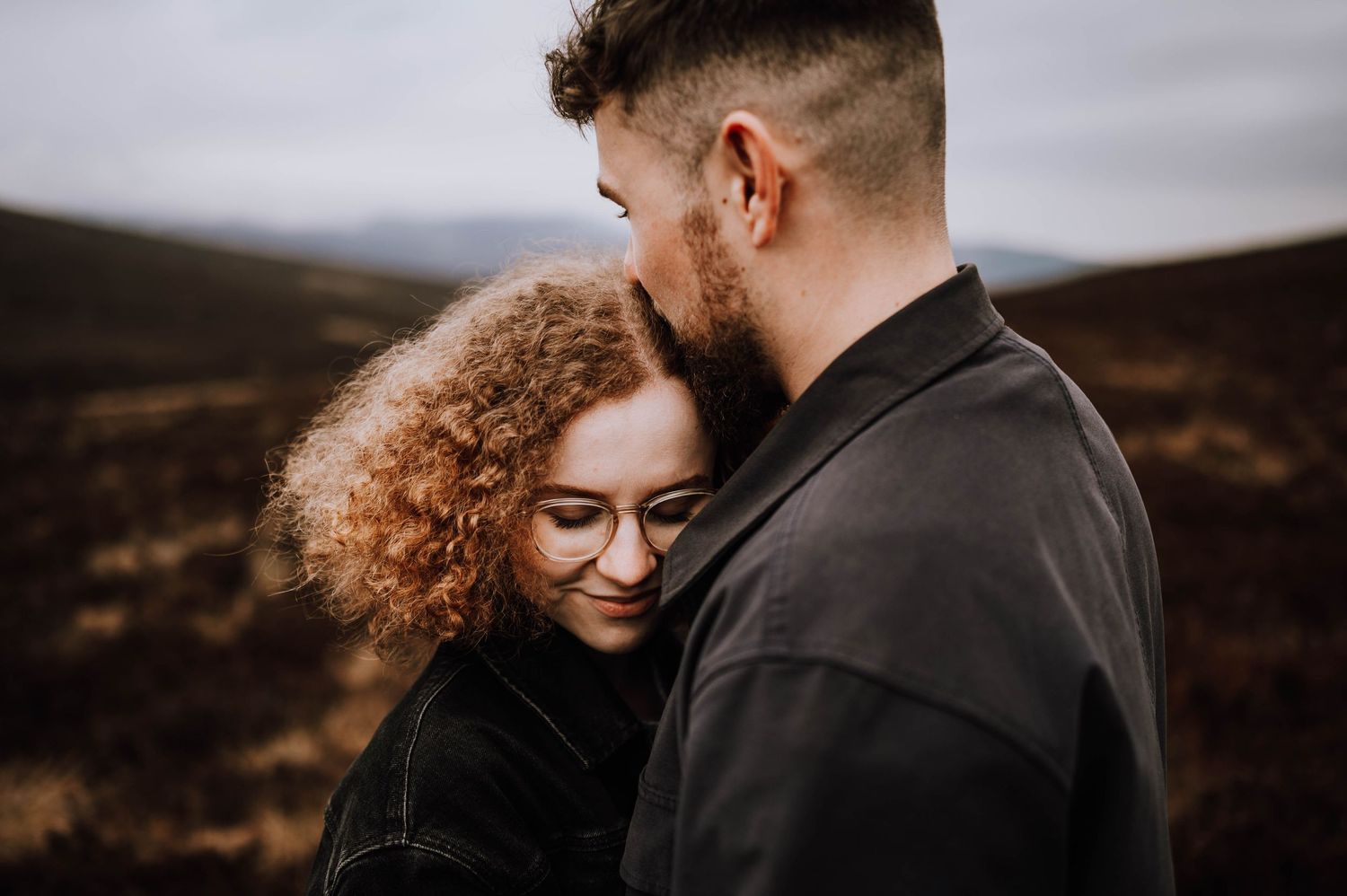 vA couple shares an intimate moment against a moody mountainous landscape at sunset.