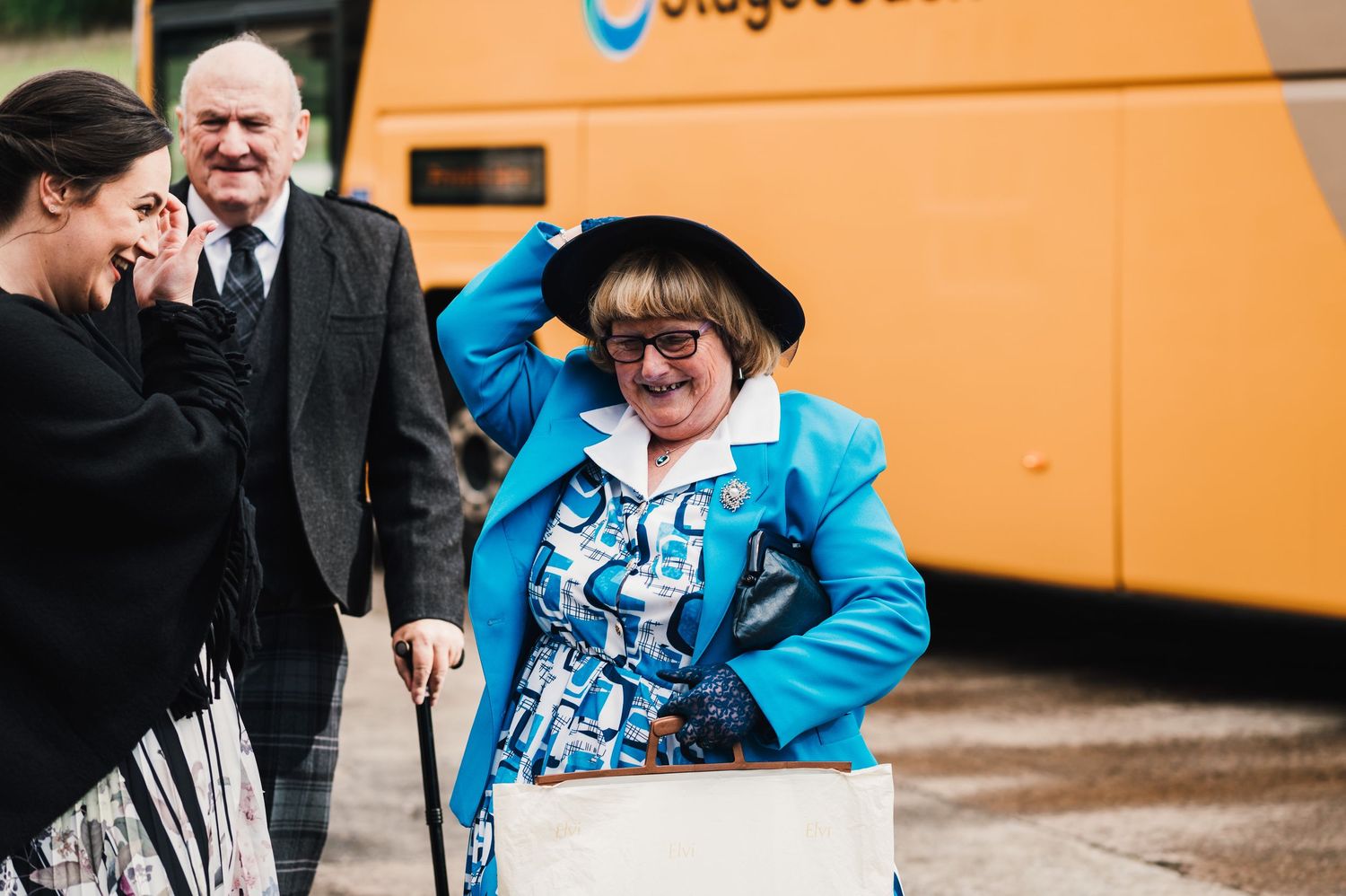 Wedding guests interacting outside near an orange coach bus.