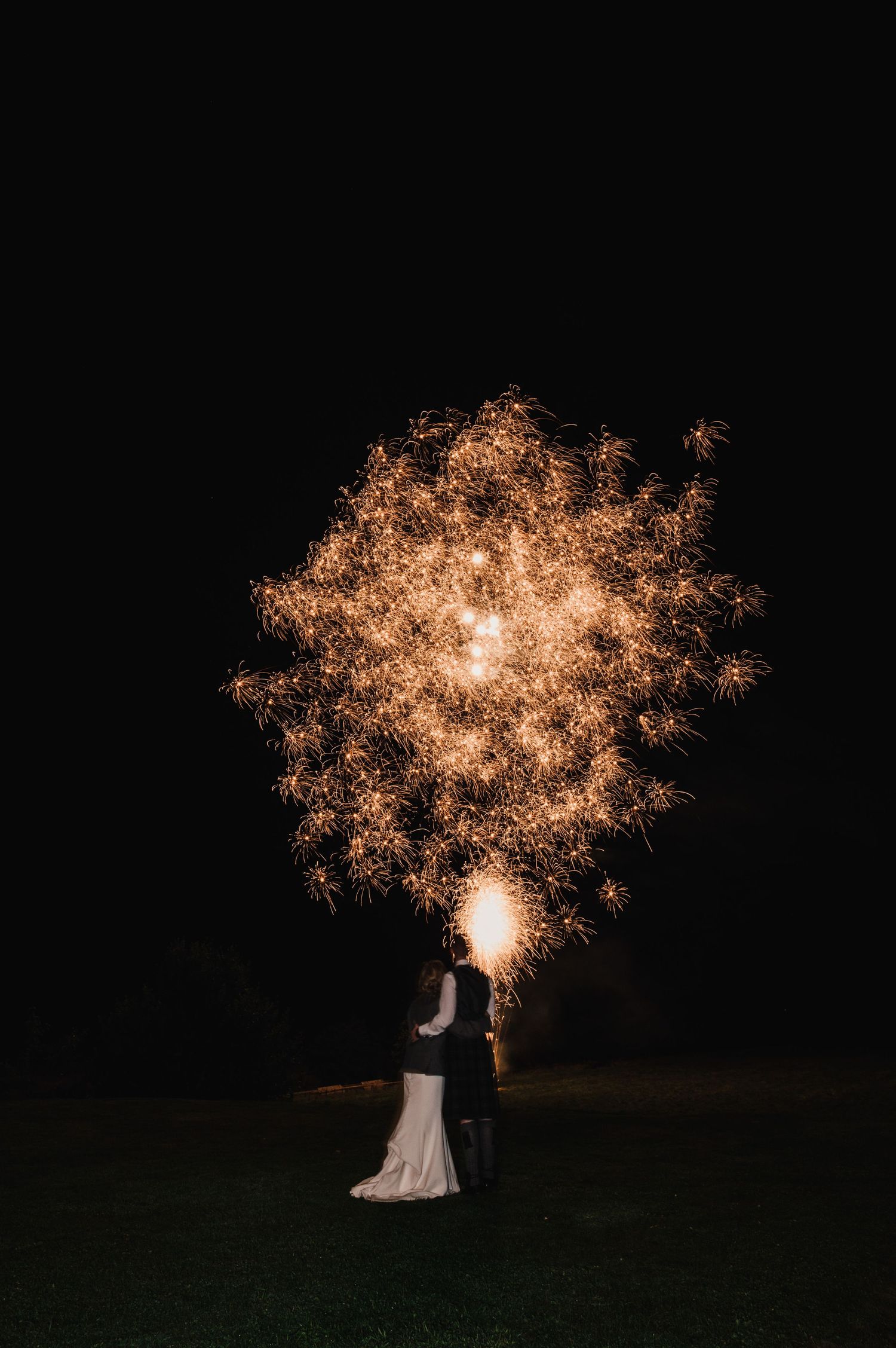 Golden fireworks display illuminates night sky behind wedding couple silhouette.