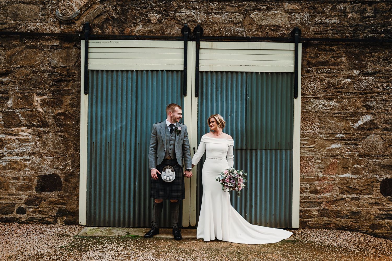 Stone wall backdrop with elegant blue doors creates a rustic setting for wedding photography.
