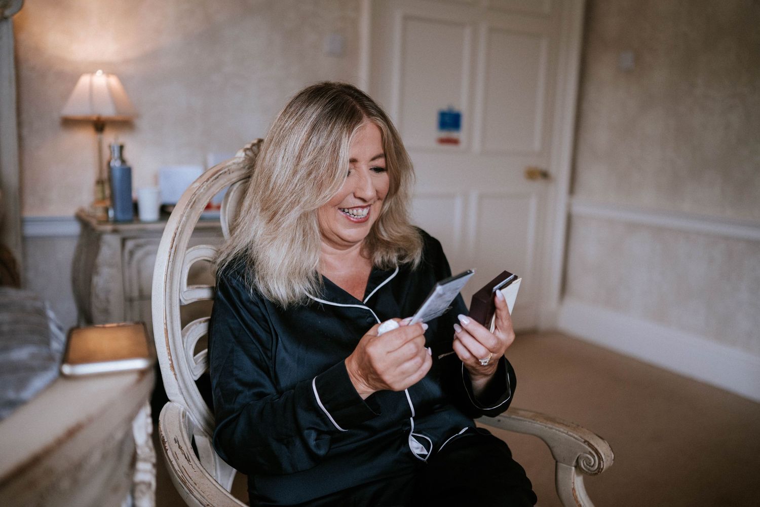 A person in a black jacket sits comfortably in a chair while looking at their mobile phone with a joyful expression.