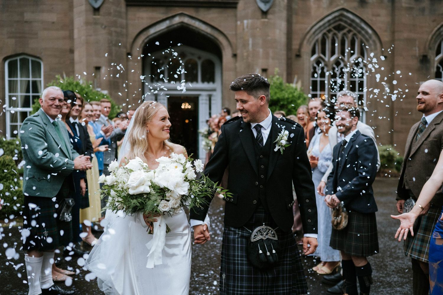 Wedding party celebrates with confetti outside a historic stone building.