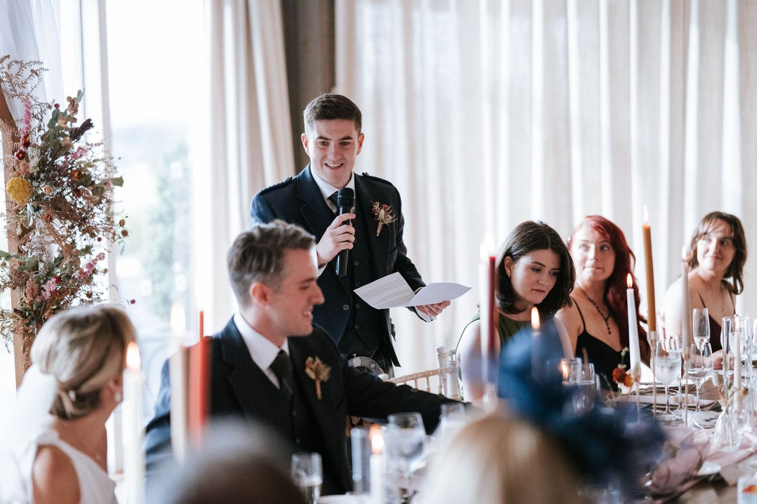 Indoor wedding reception with white drapes and natural lighting streaming through windows.