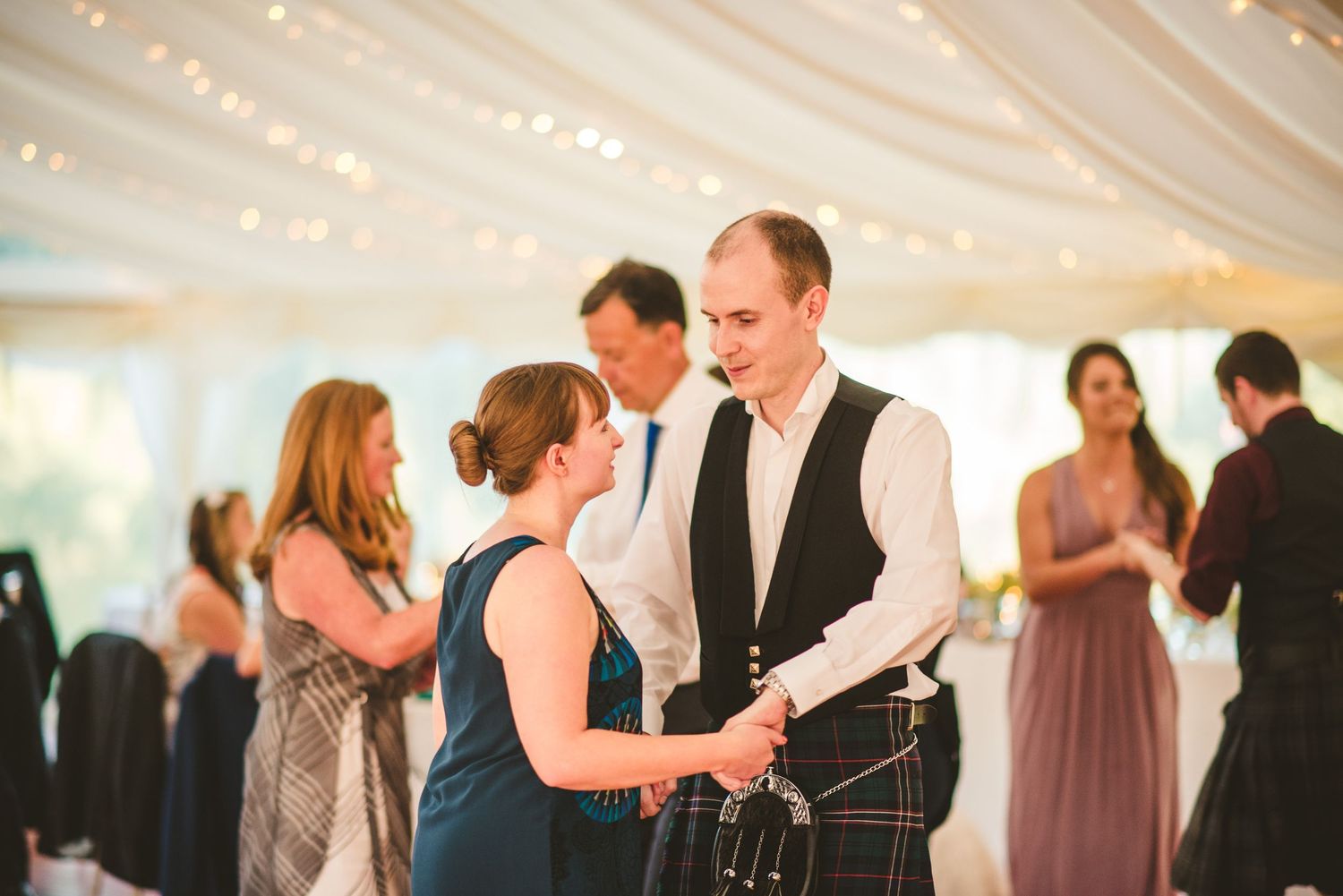 Wedding celebration in an elegant white tent with string lights overhead.