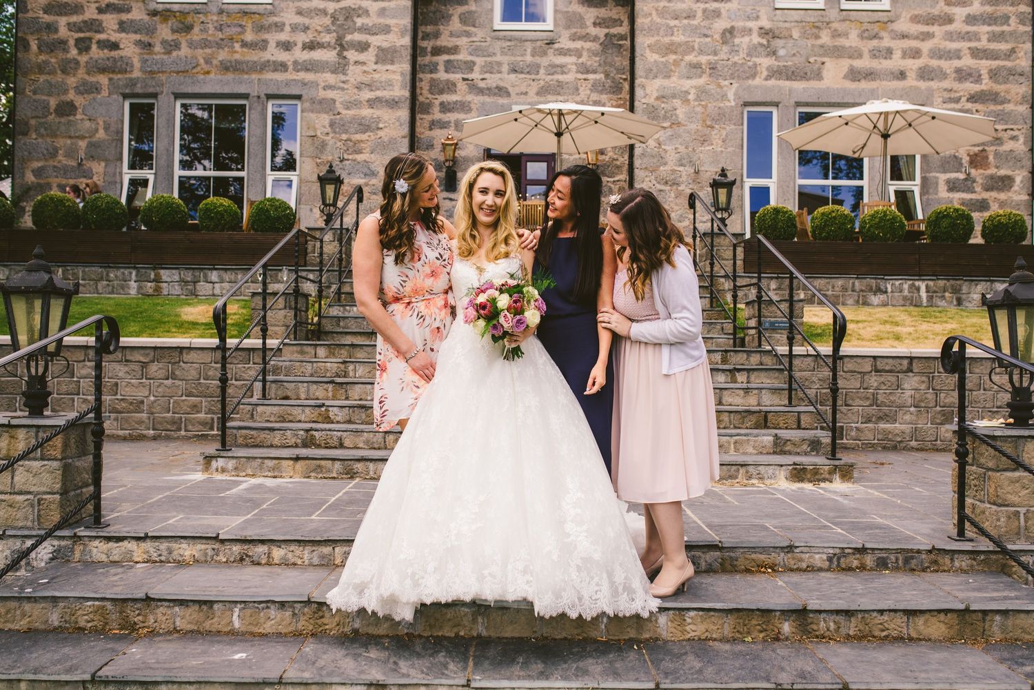 Wedding party members stand in front of rustic stone wall for formal photos.