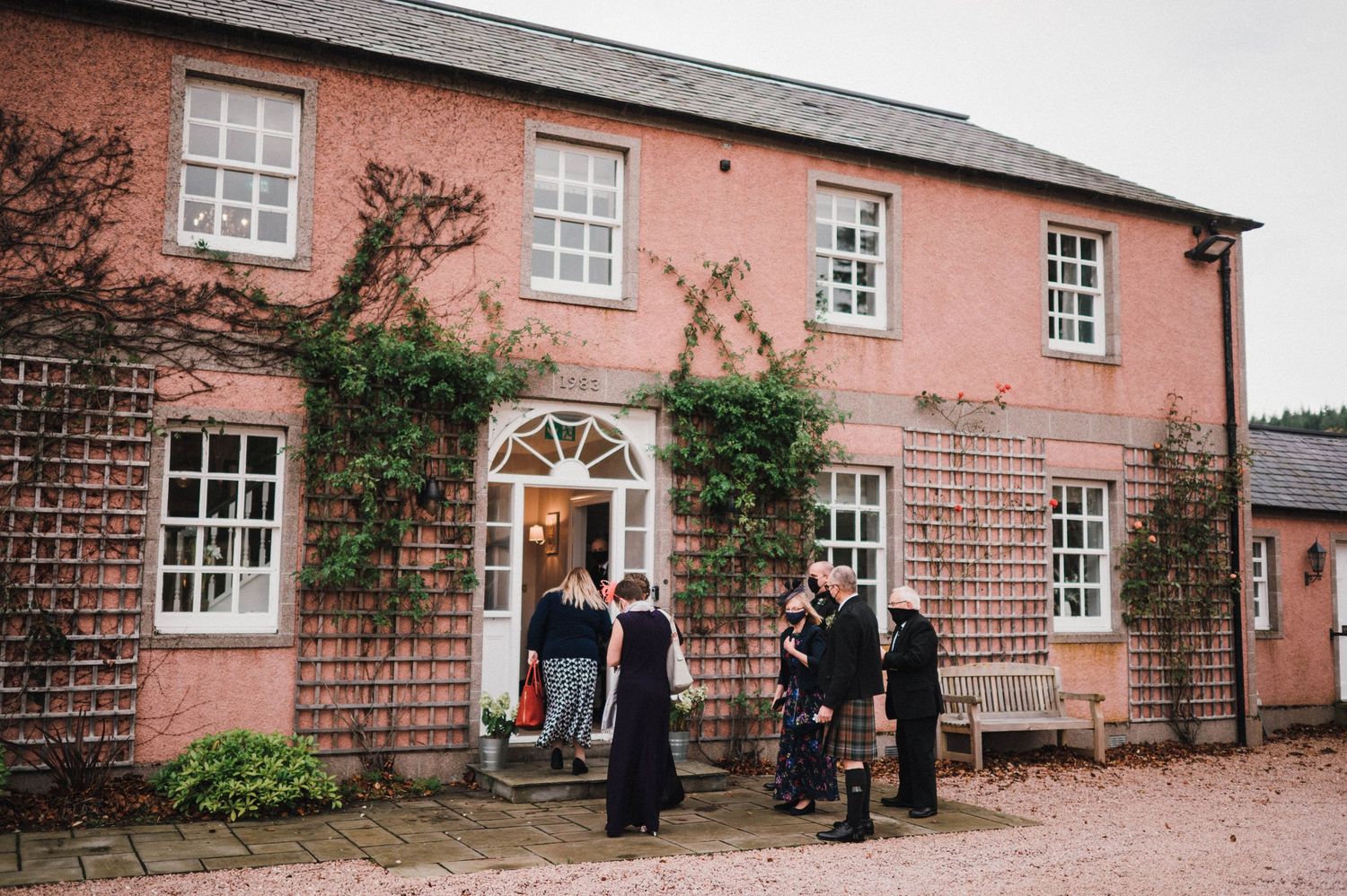 A pink Georgian-style building entrance with climbing vines and several people gathered at the doorway.
