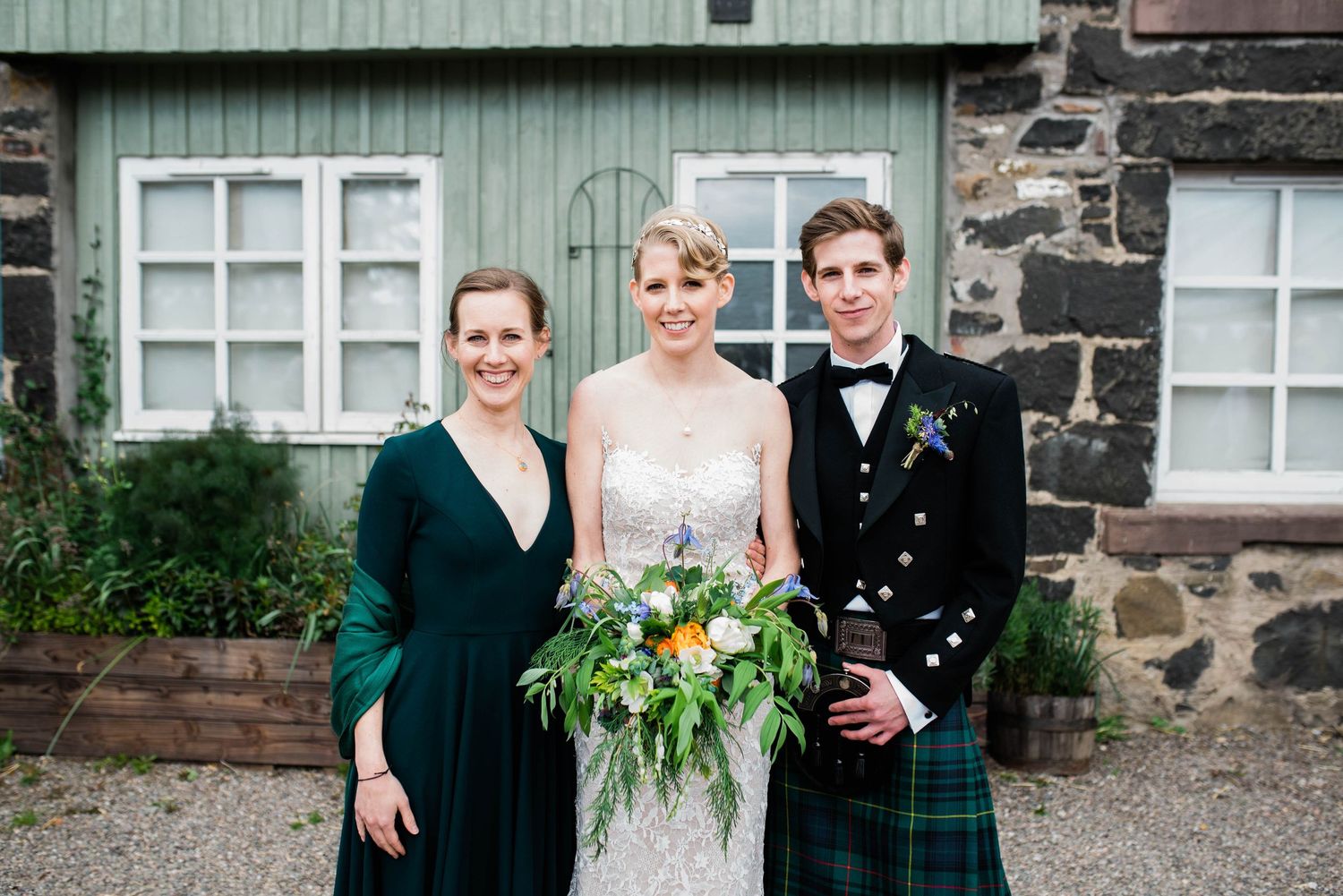 Small wedding group portrait in front of stone building with Scottish kilts and formal dress.