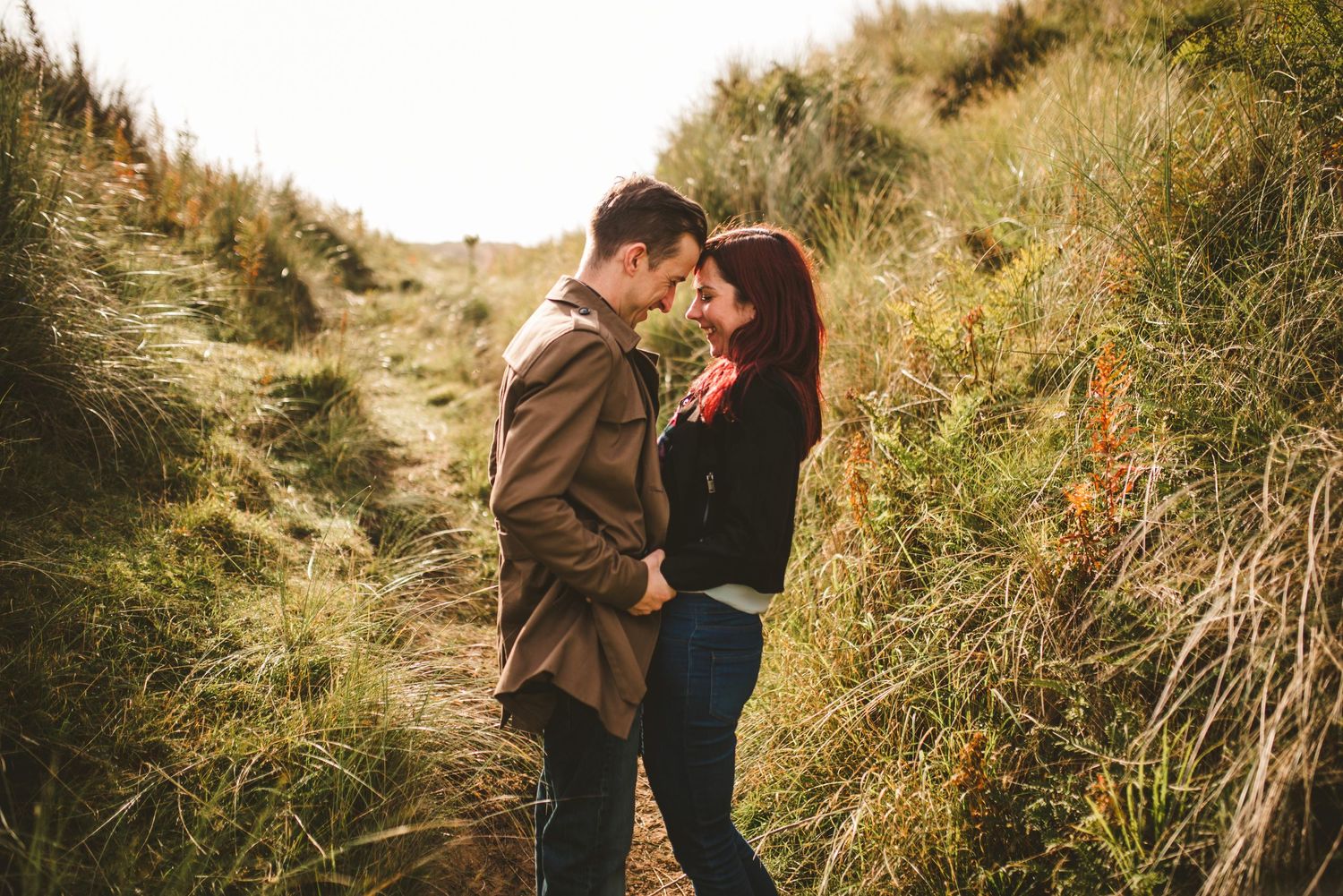 A tender moment shared between a couple on a grassy hillside path.