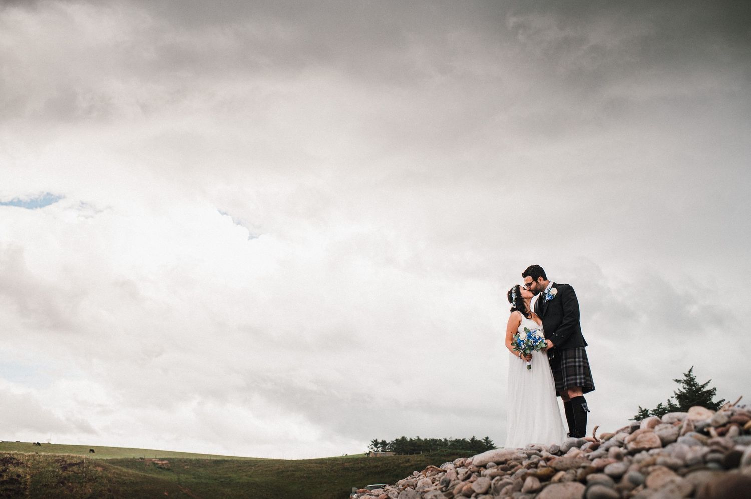 A Scottish wedding photograph taken on rocky terrain with dramatic cloudy skies.