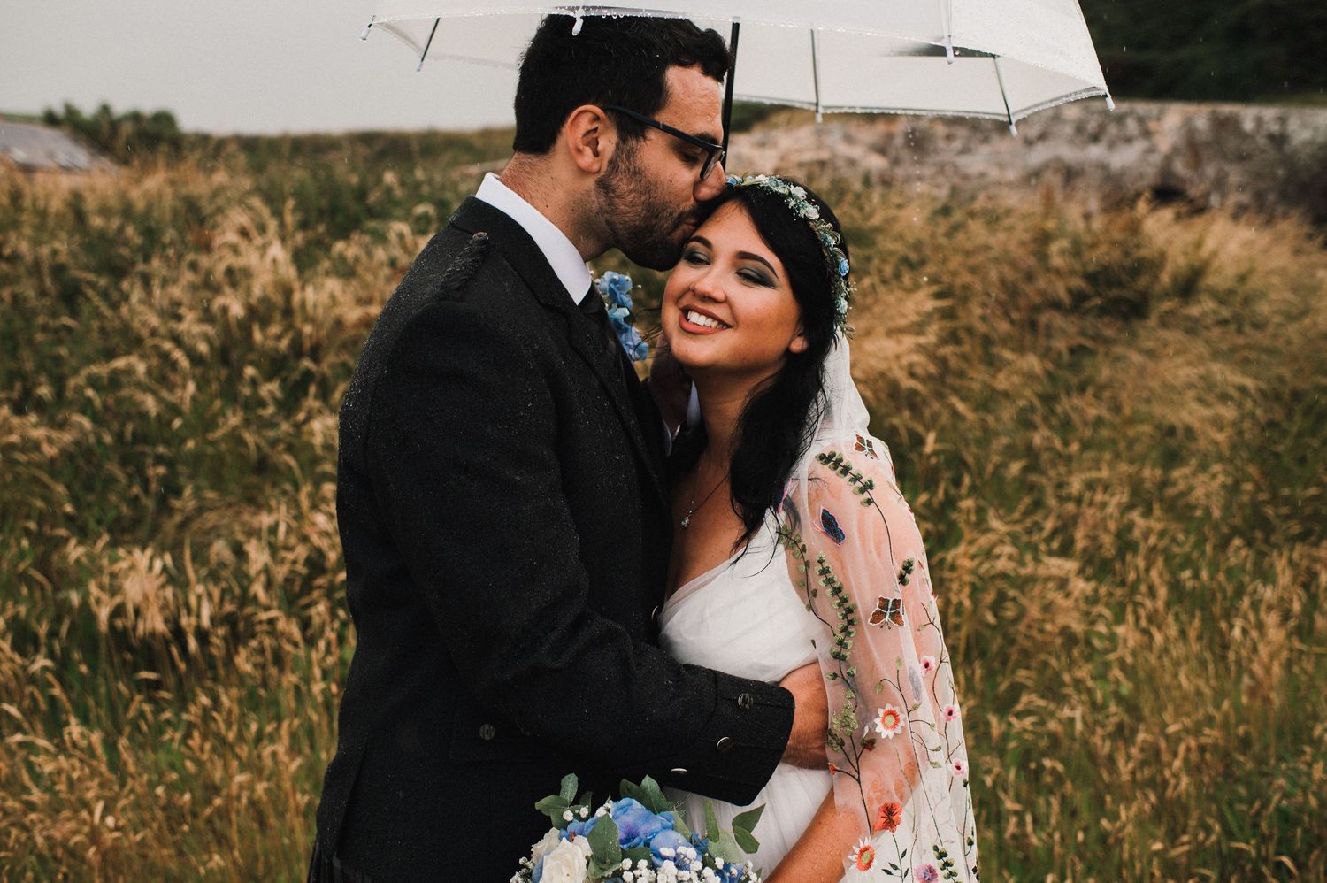 A tender moment between newlyweds in a golden field with blue floral bouquet.