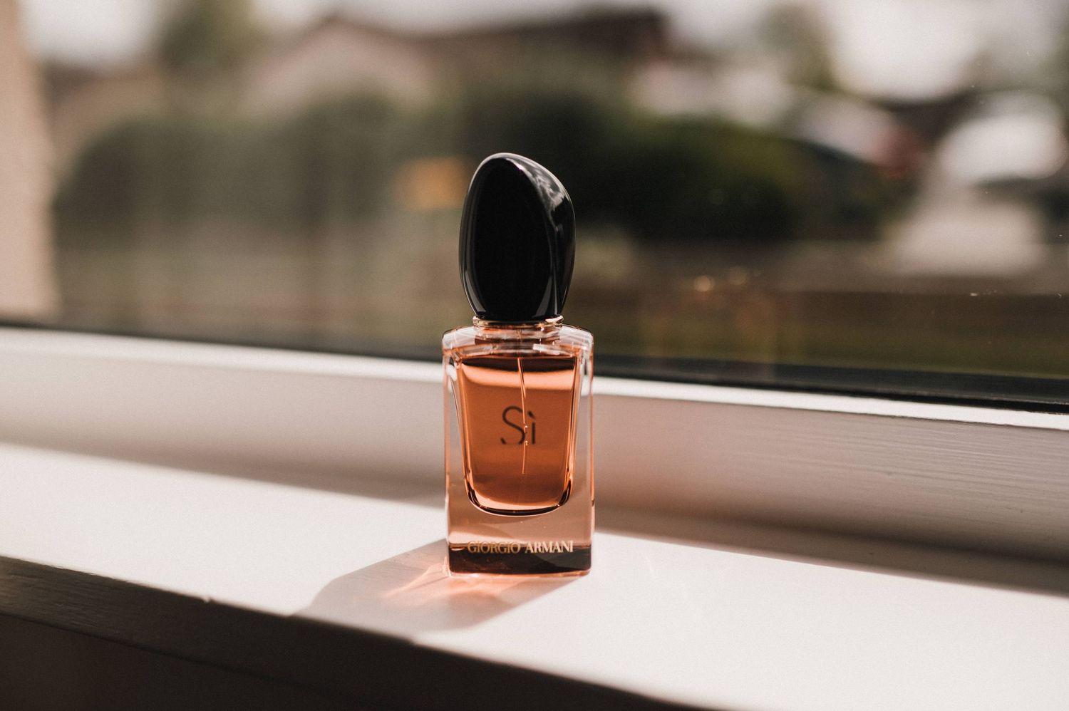 A small perfume bottle sits on a windowsill in warm natural lighting.