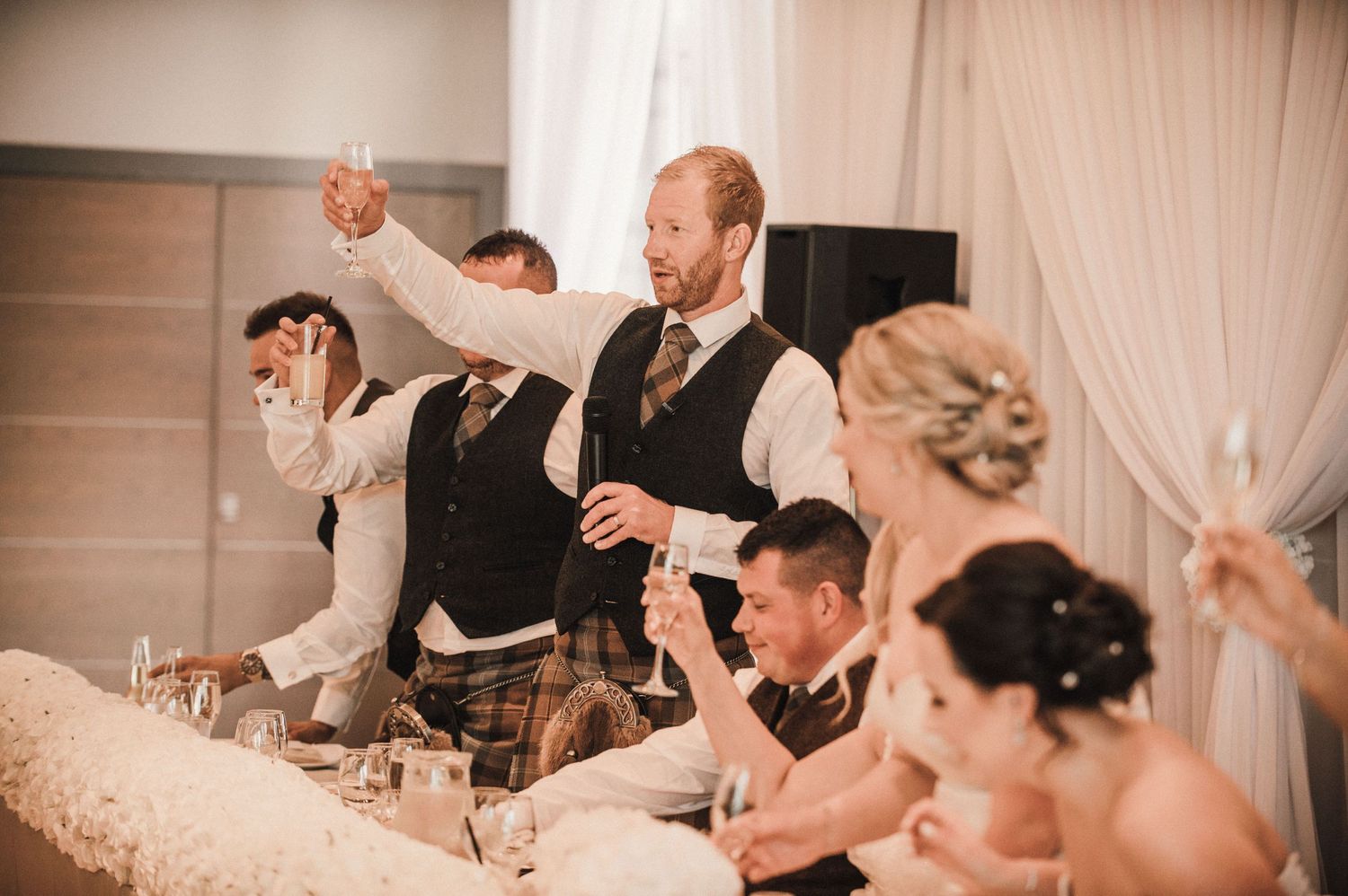 Wedding party raises glasses in celebratory toast at elegant reception venue.