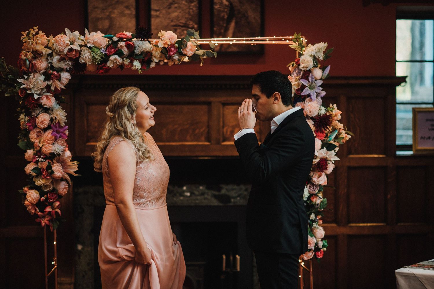 A touching exchange of vows beneath a floral arch during an indoor ceremony.