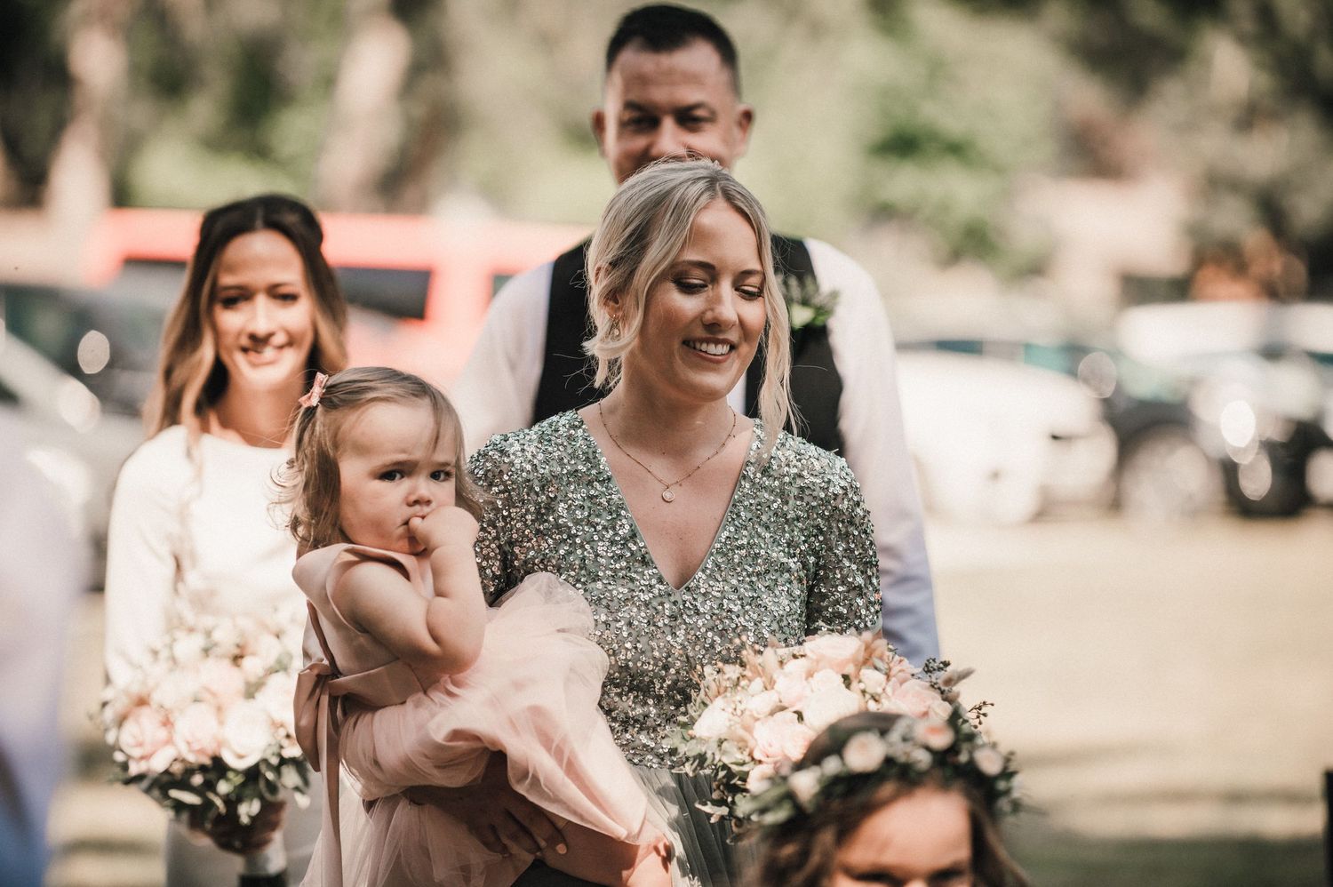 Wedding party members gather outdoors holding bouquets during celebration.