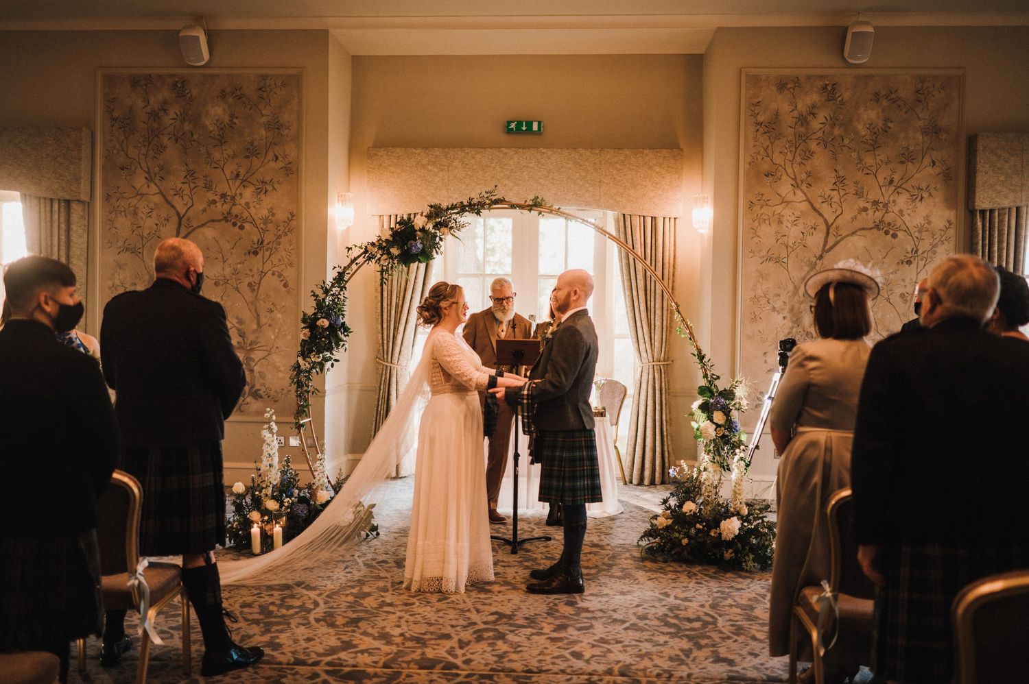 Wedding ceremony in an elegant room with floral arch and guests seated in rows.
