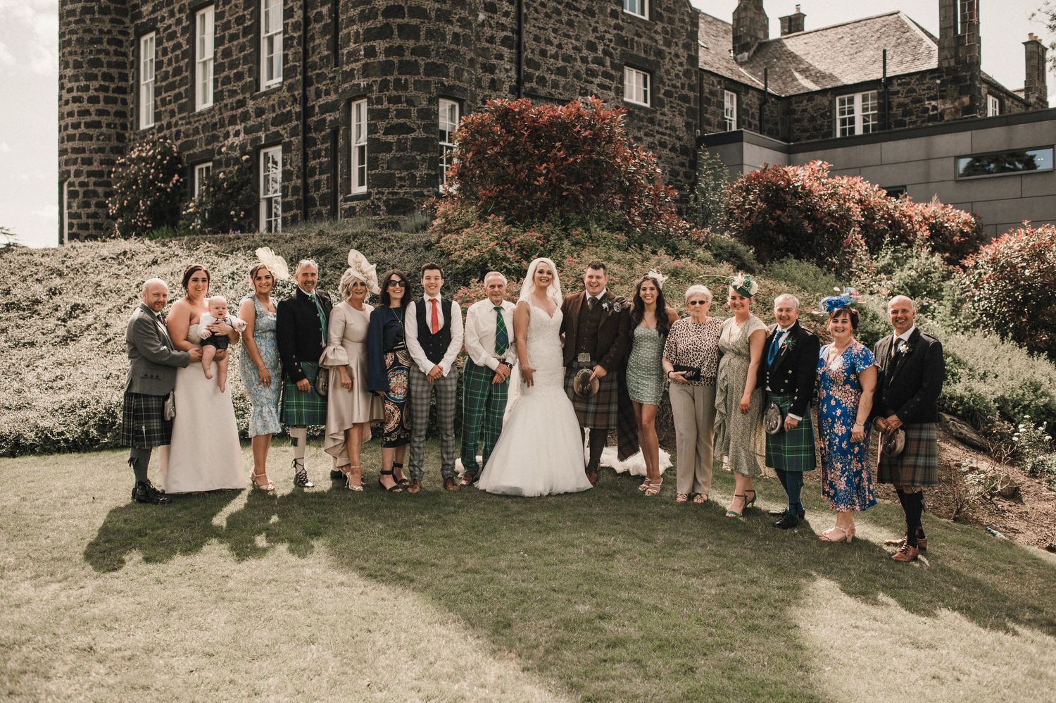 Aerial view of large wedding party gathered on grass forming a heart shape.