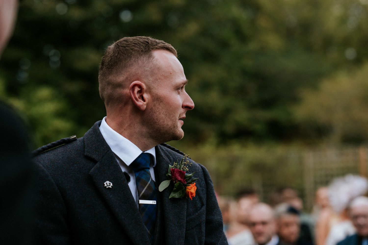 Guests gather outdoors for a wedding ceremony in a garden setting.