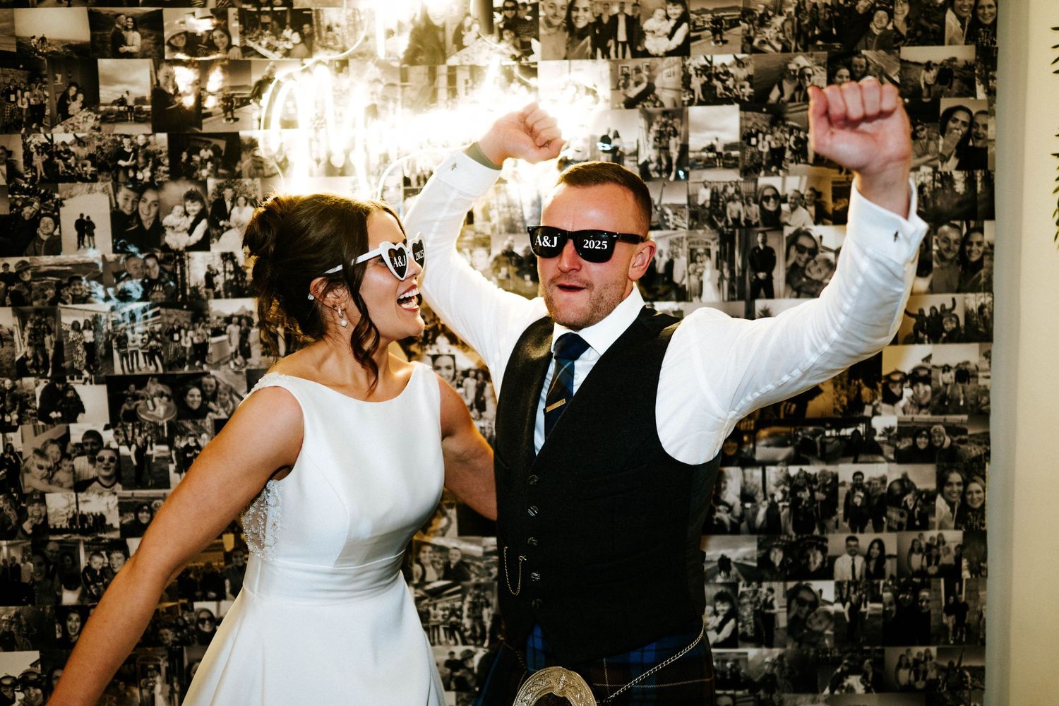 Wedding couple dancing and celebrating against a photo wall backdrop.