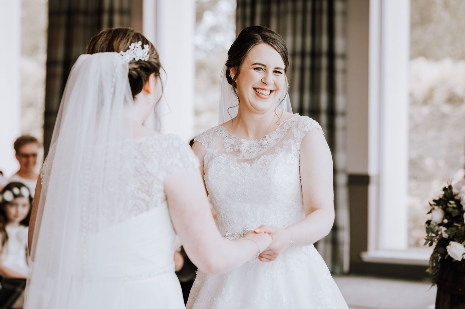 Two brides in lace wedding dresses share a happy moment during their wedding ceremony.