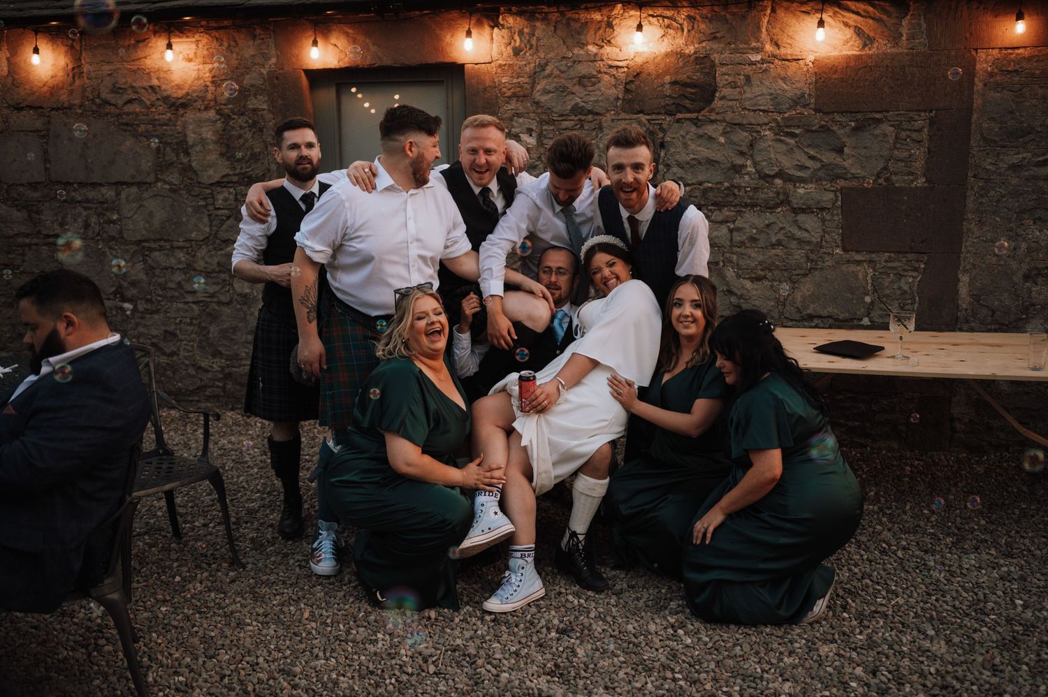 Wedding party posing together in a rustic outdoor setting with stone walls.