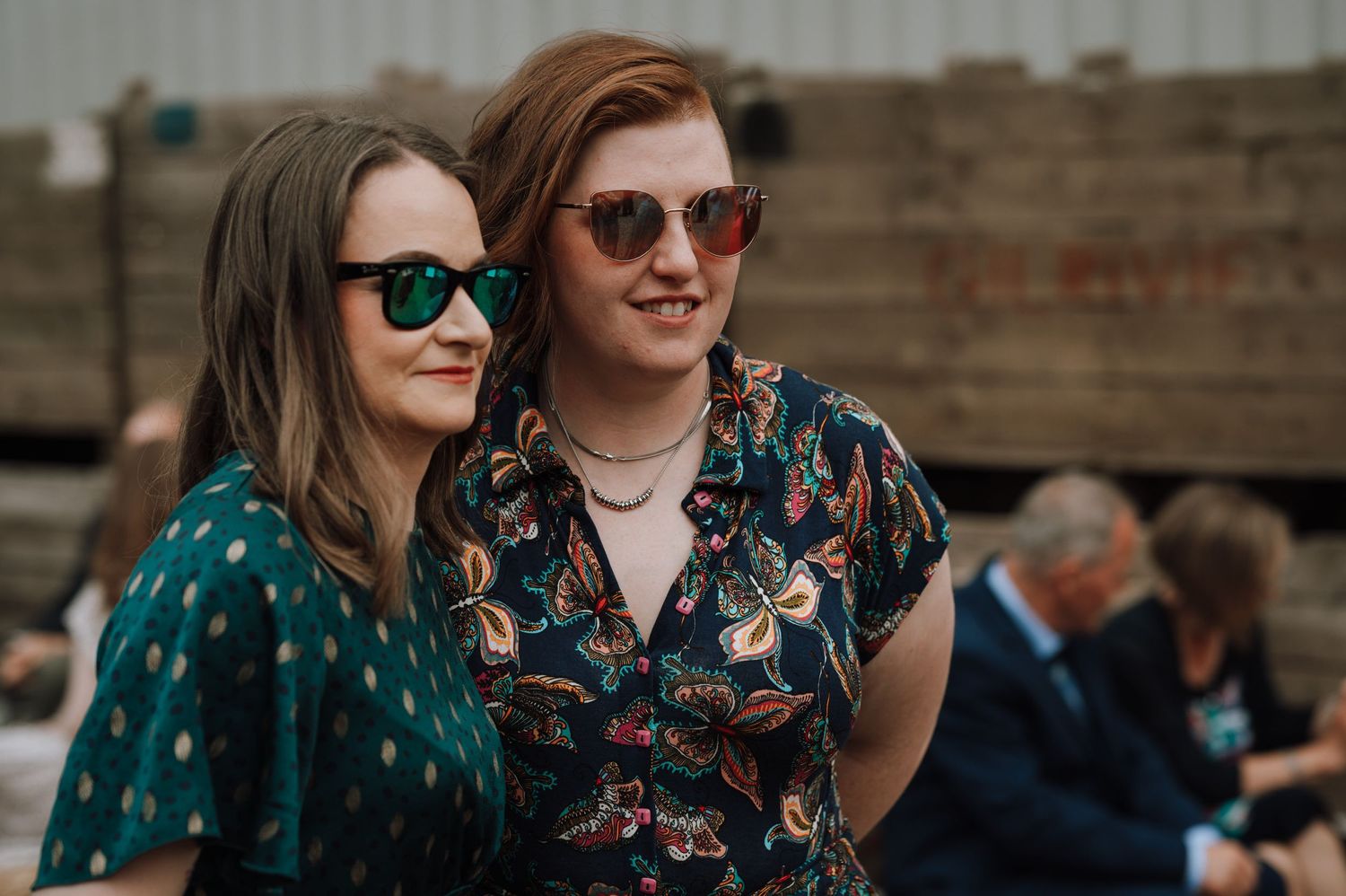 Wedding guests in colorful attire and sunglasses enjoying outdoor celebration.
