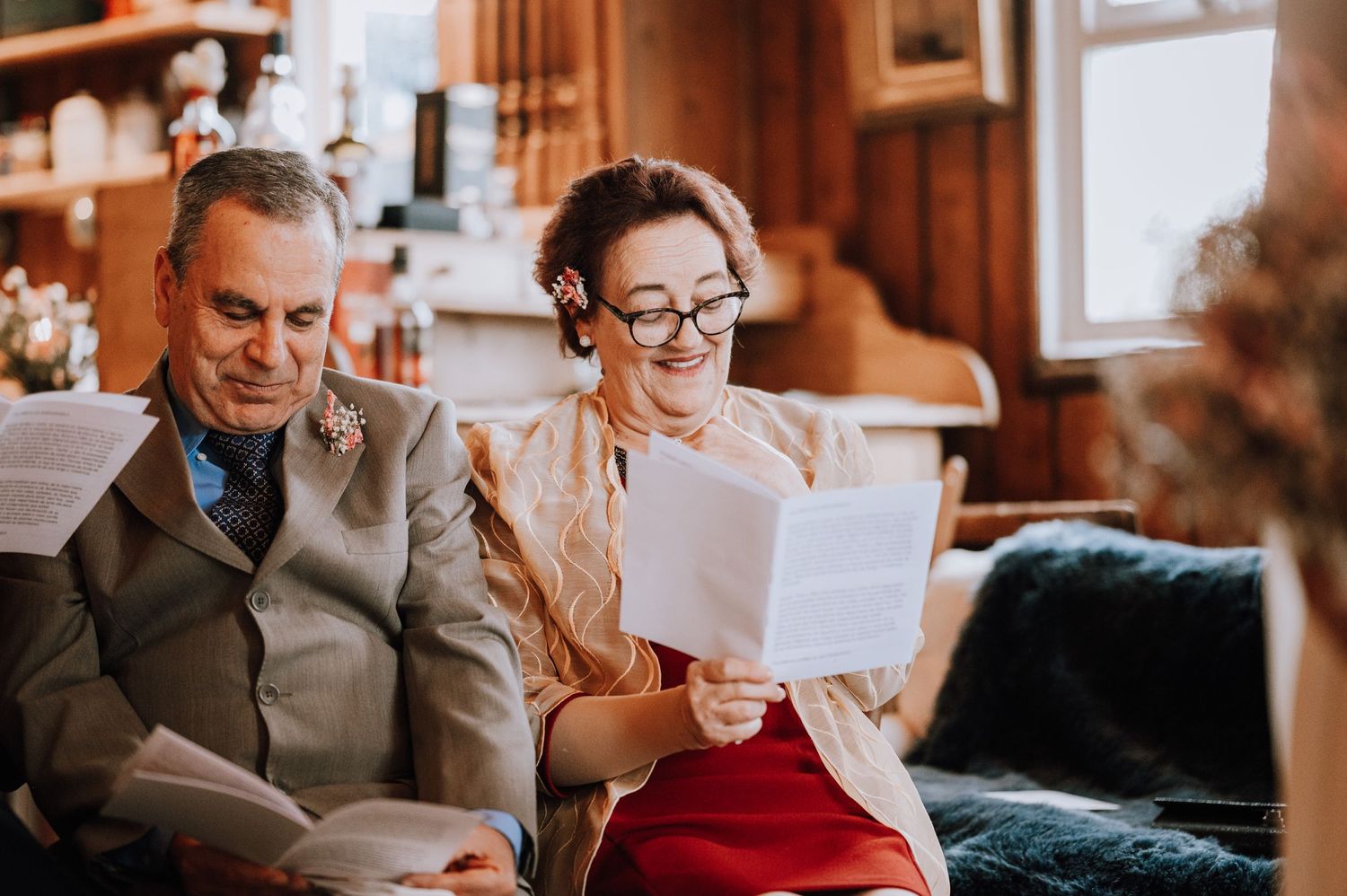 Two guests smile while reading from papers during an indoor celebration.