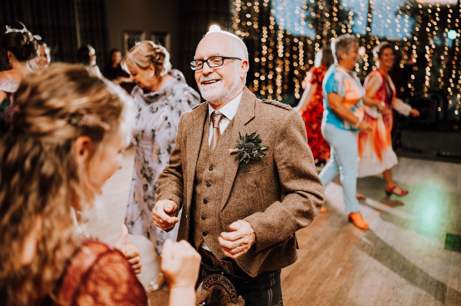 A person in a tan suit dances enthusiastically at a wedding reception.