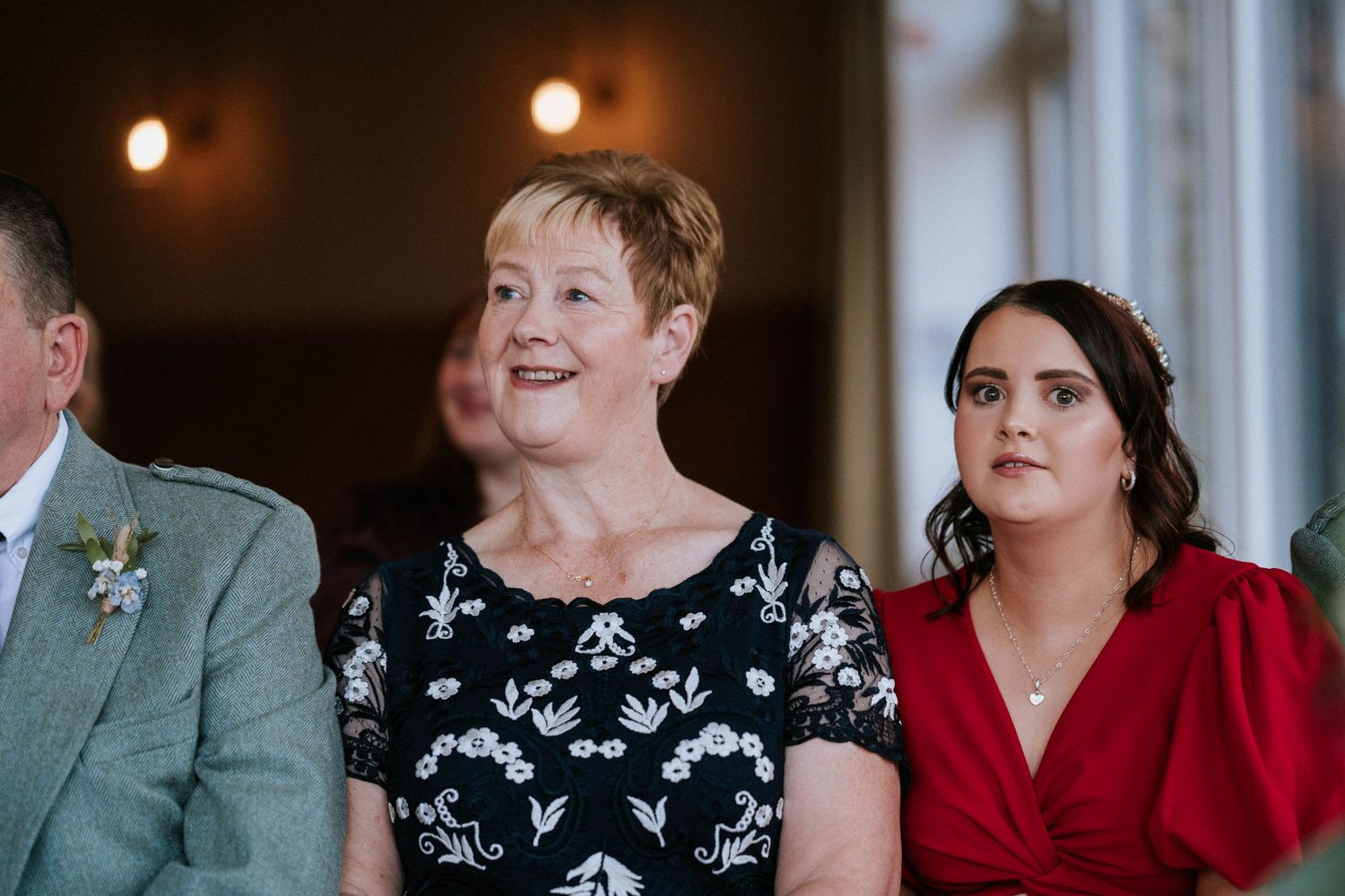 Wedding guests seated at tables in an indoor reception venue with warm lighting and elegant decor.