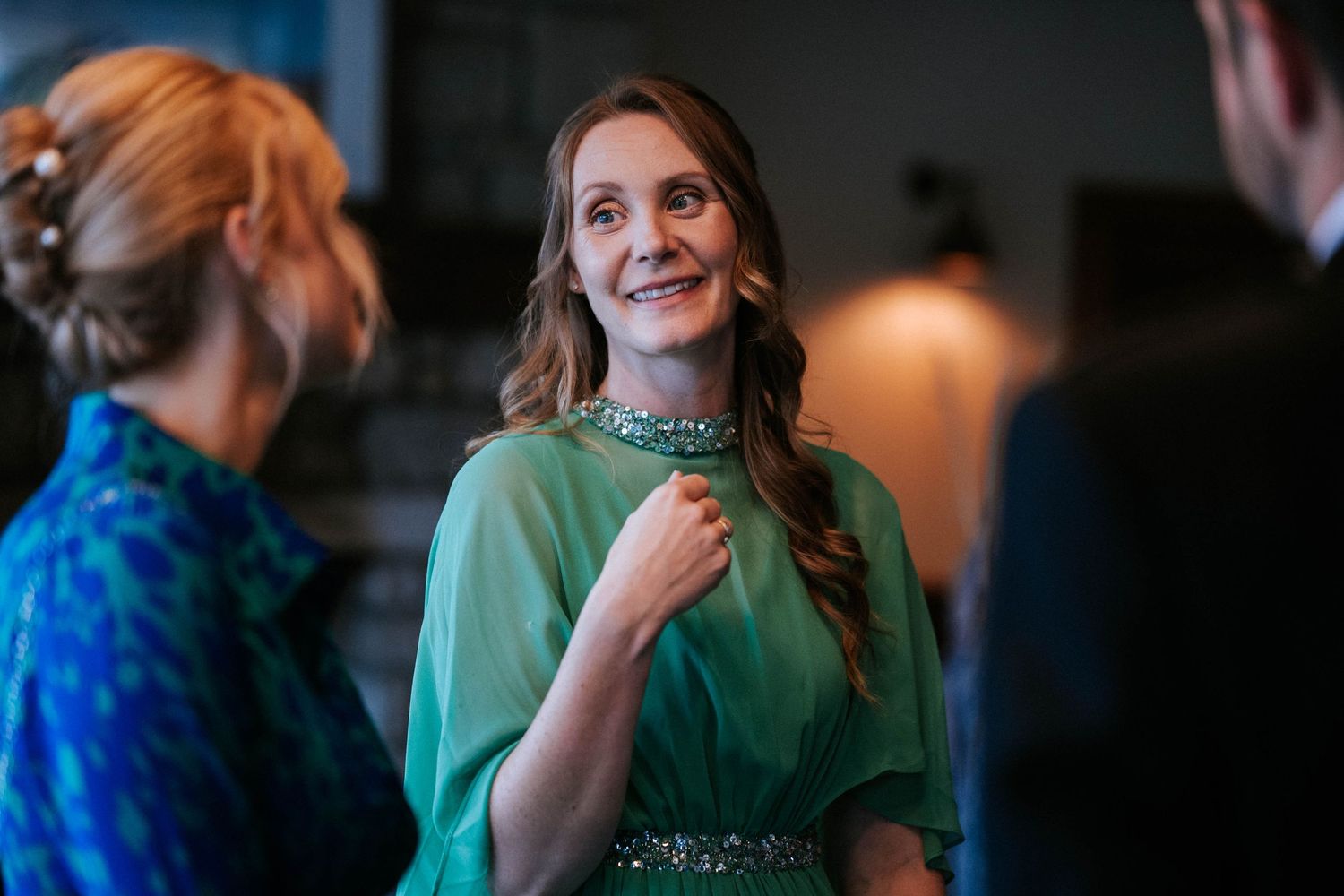 People gathered at an evening event with someone wearing an emerald green dress in focus.