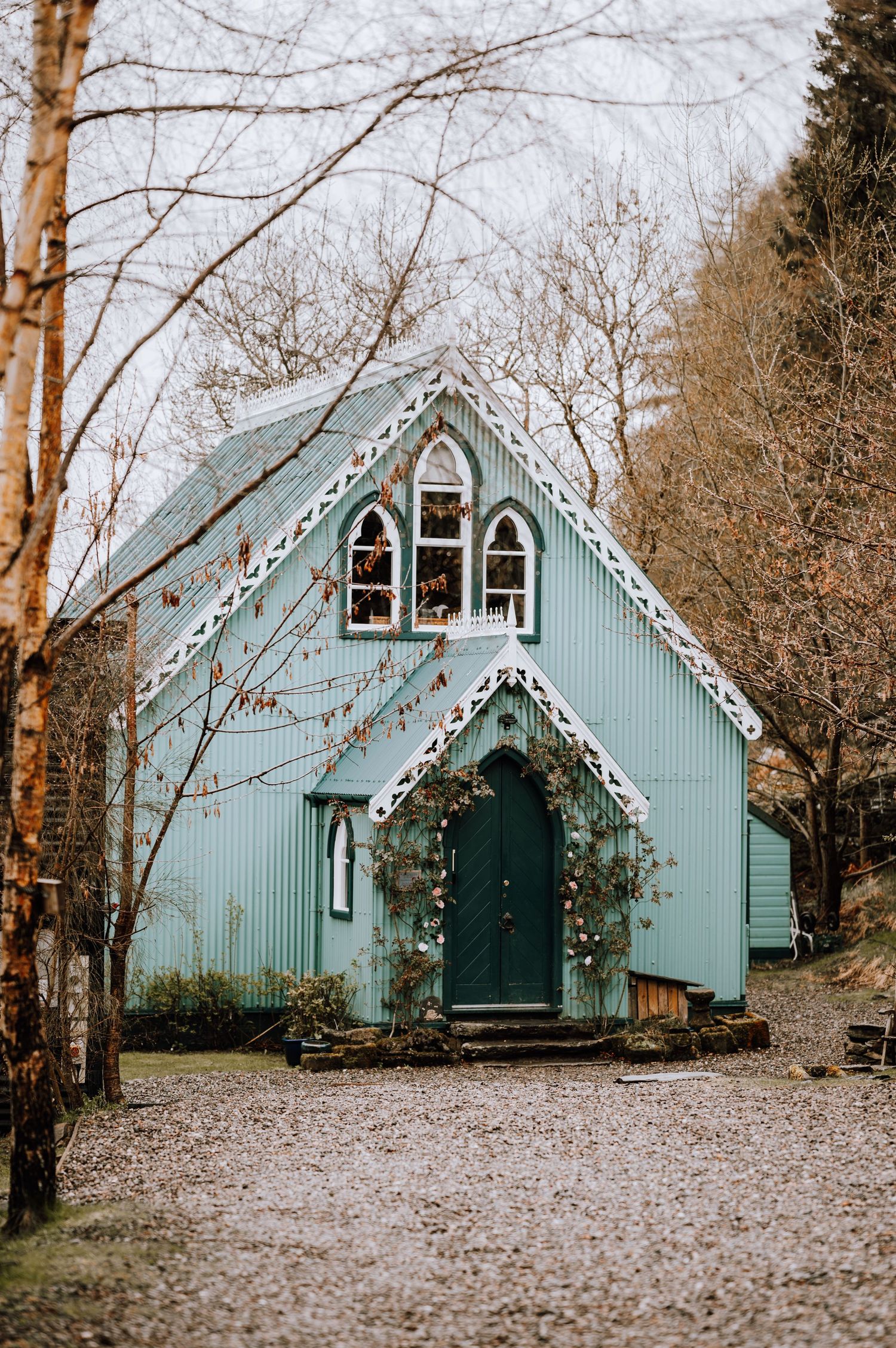 A quaint mint-green chapel with Gothic windows and ornate trim surrounded by bare winter trees.