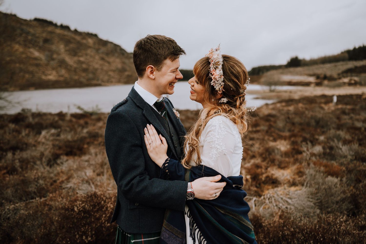 Couple shares romantic moment against dramatic coastal Scottish landscape.