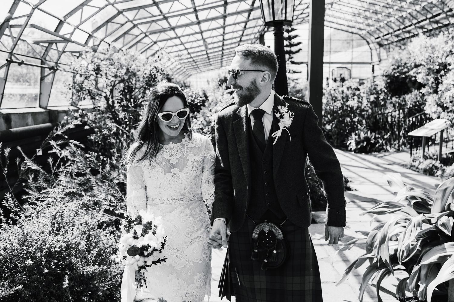 Black and white wedding photo captured in a light-filled greenhouse filled with lush plants.