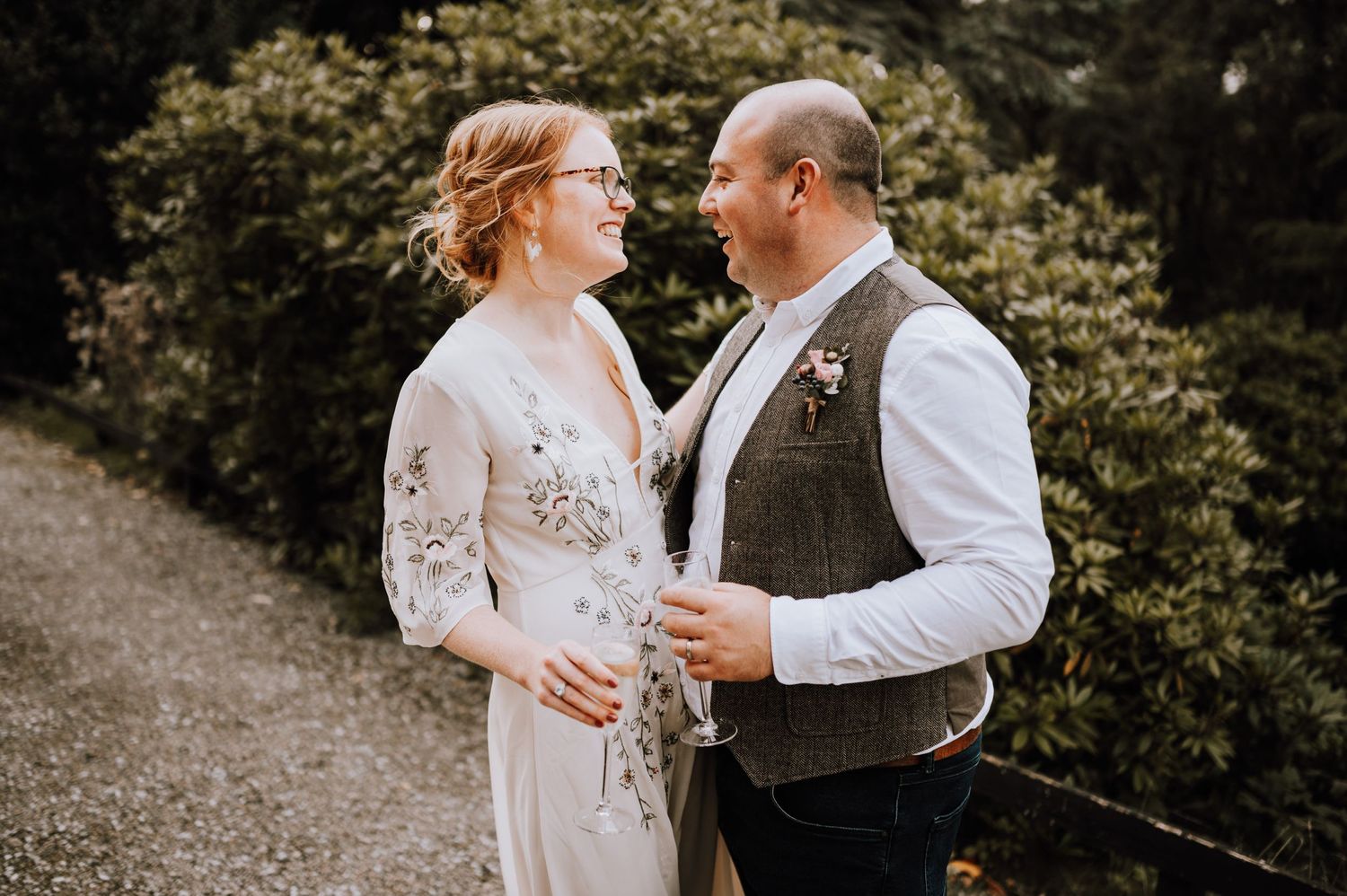 Couple in elegant wedding attire sharing intimate moment on garden path.