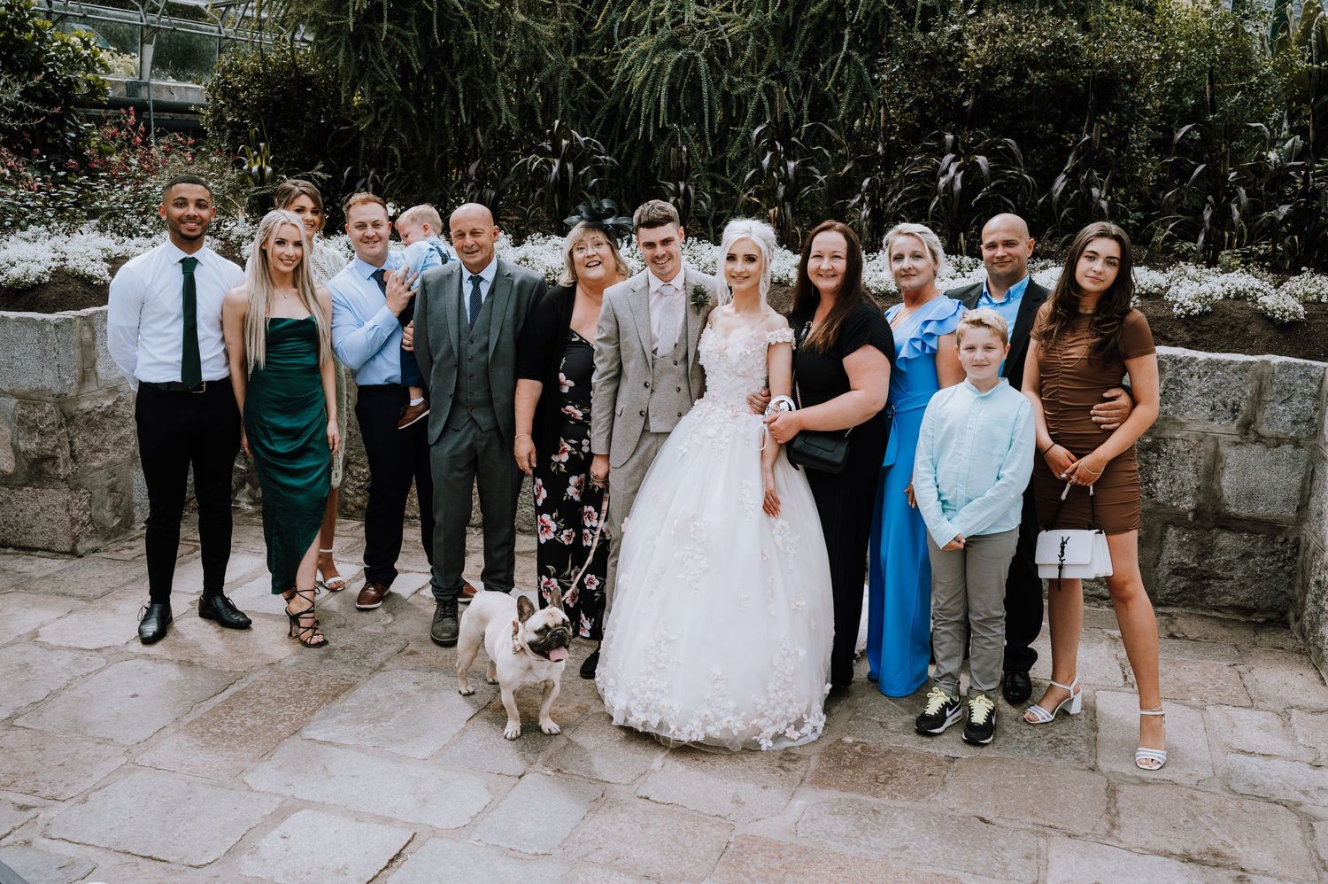 A large wedding party gathered outdoors with their dog for a group photo.