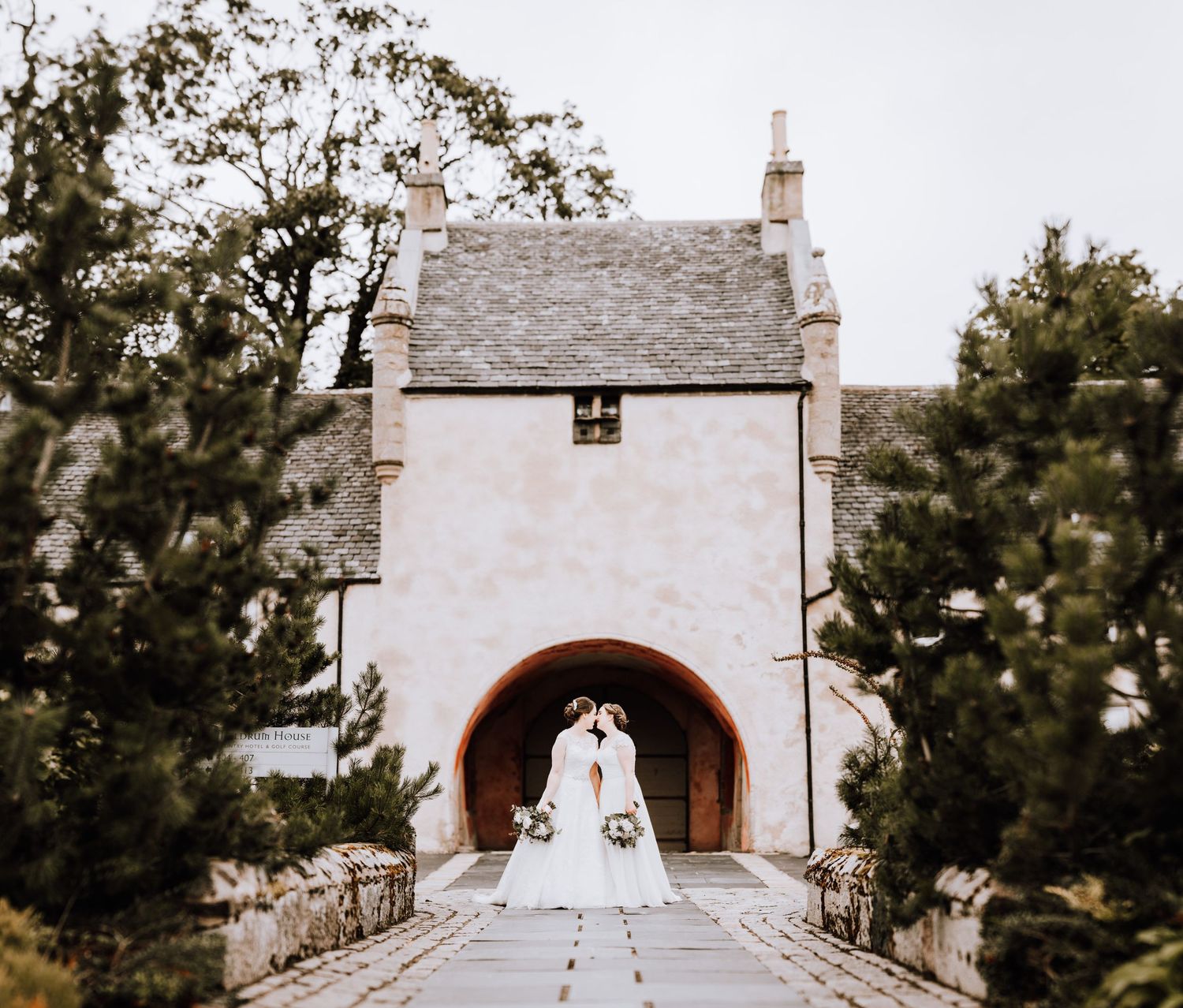A romantic wedding photo framed through a stone archway entrance of a historic building.