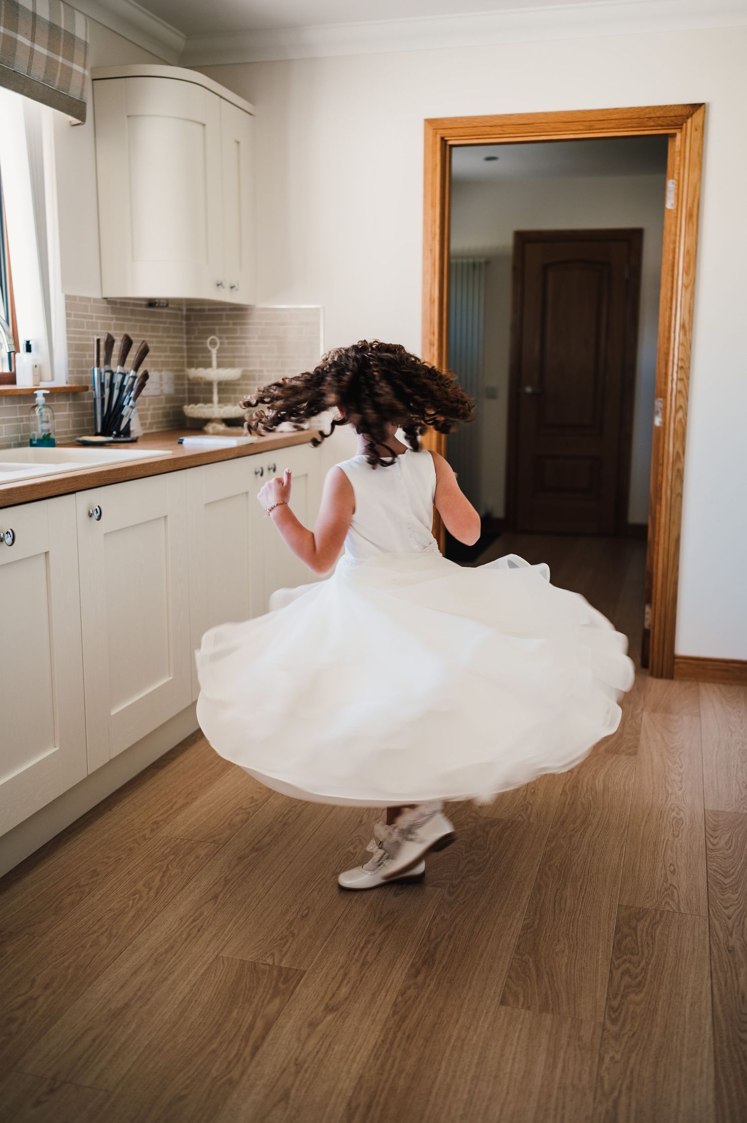 Young attendant in white dress twirling in kitchen showing off the flowing layers.