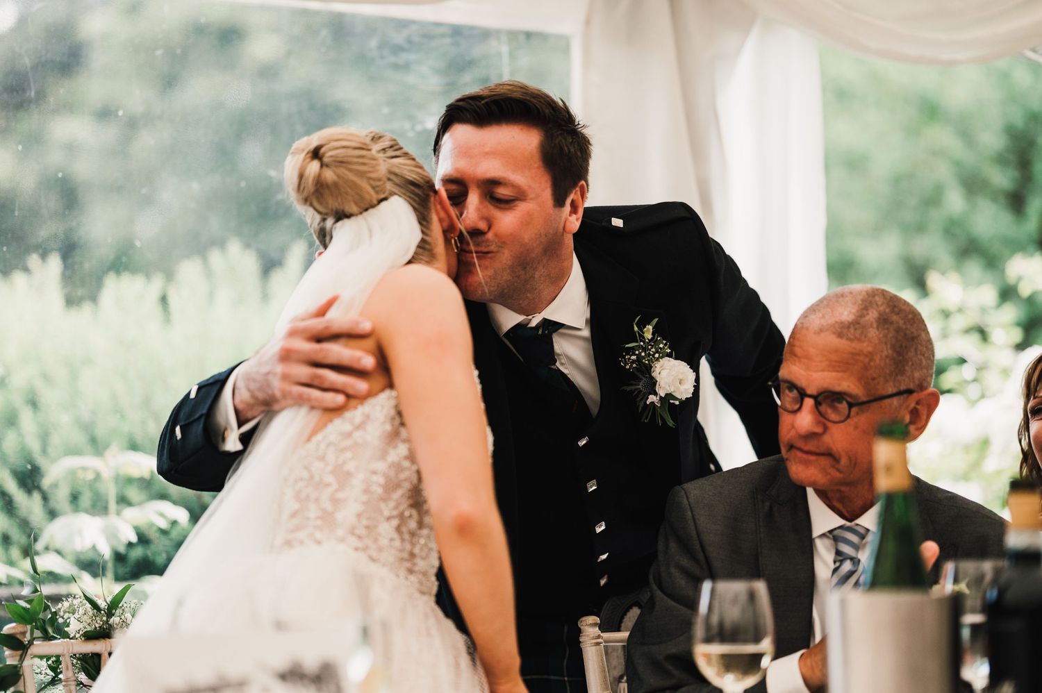Emotional moment during wedding speeches at elegant tented reception with formal table settings.