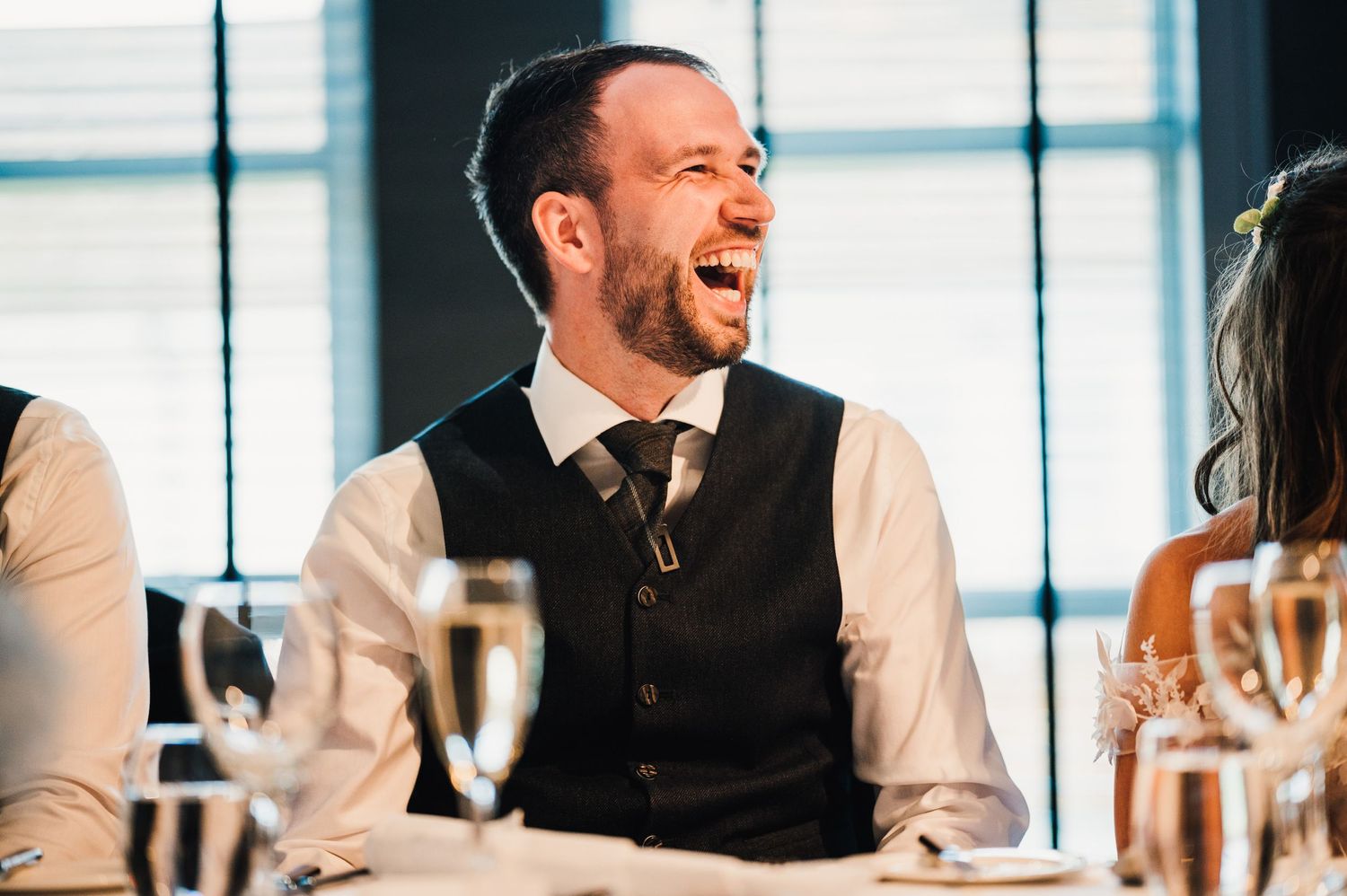 A guest in formal attire laughs during a wedding reception.