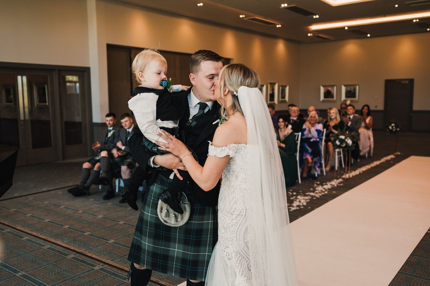 A wedding celebration in an indoor venue with traditional Scottish dress and formal attire.