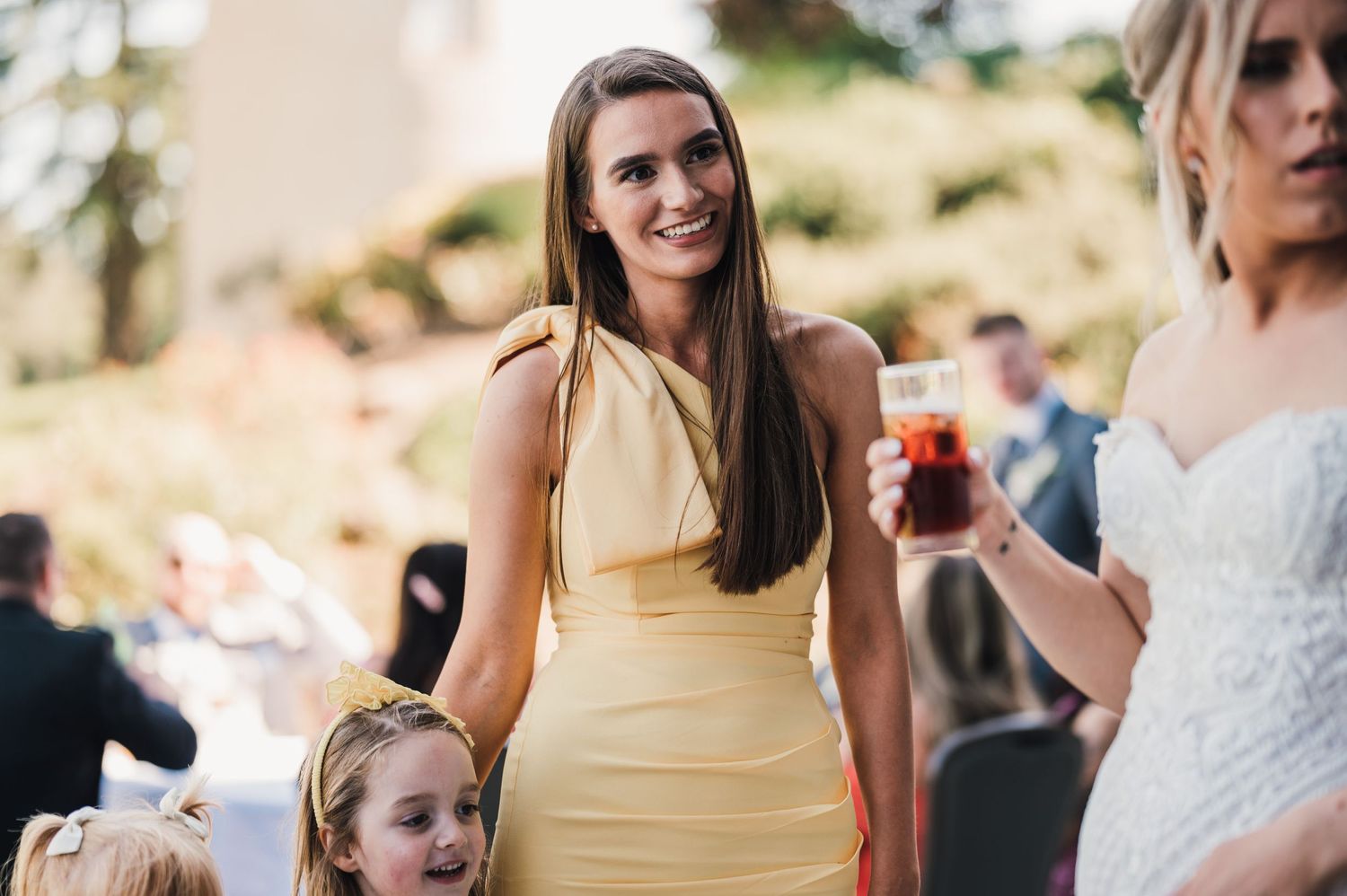 Wedding guests gathered outdoors during a celebration with people in yellow and white dresses.