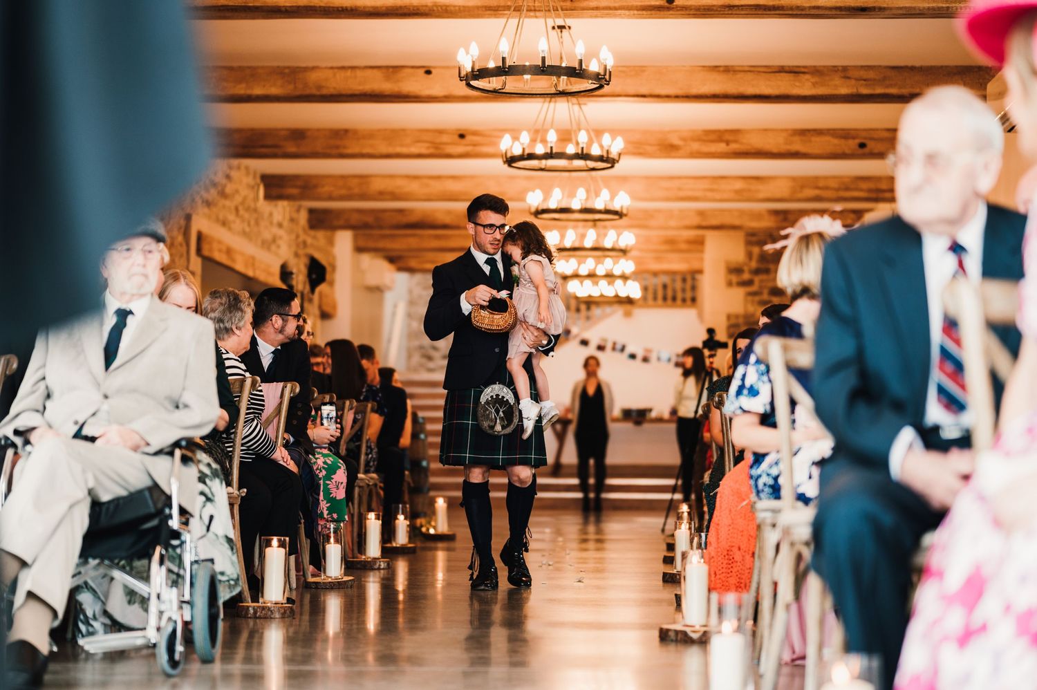 Traditional Scottish wedding processional in a rustic venue with wooden ceiling beams and chandeliers.