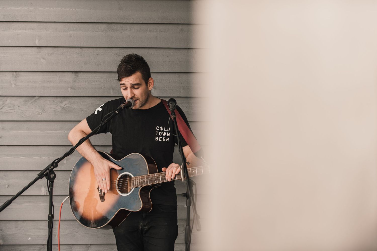 A musician performs with an acoustic guitar against a grey wall backdrop.