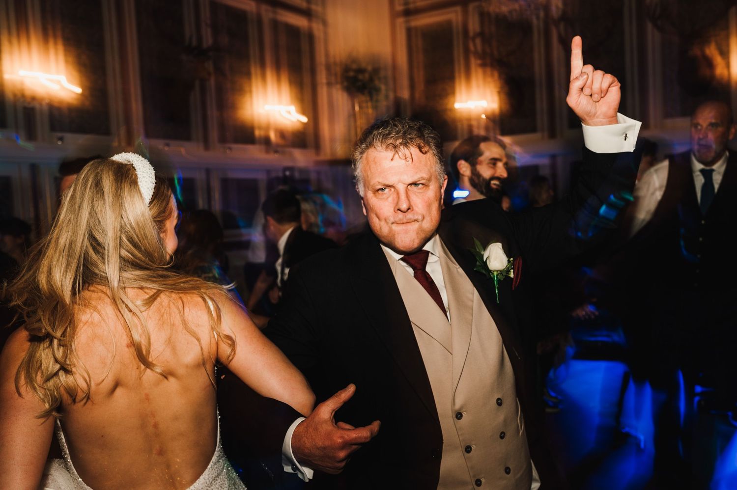 Wedding guests dancing enthusiastically at a formal reception with mood lighting.
