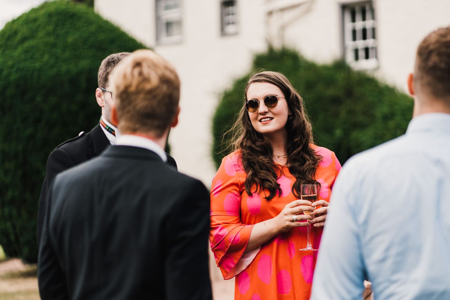 Wedding guests in formal attire socialize on garden lawn during reception.