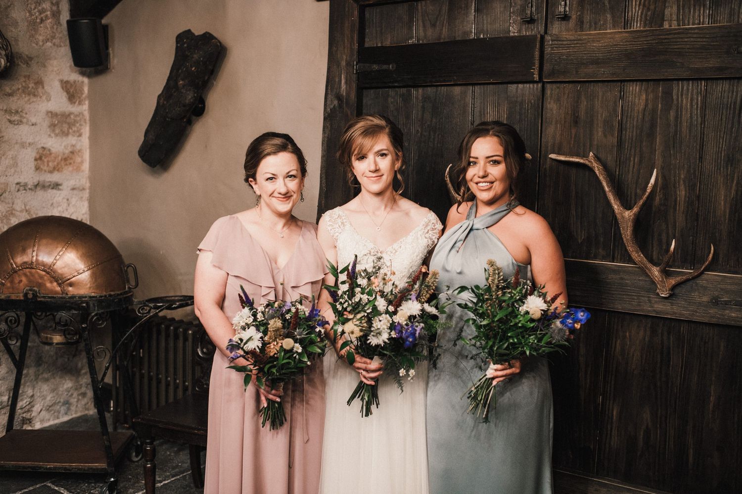 Wedding party members hold colorful bouquets while posing in front of rustic decor.